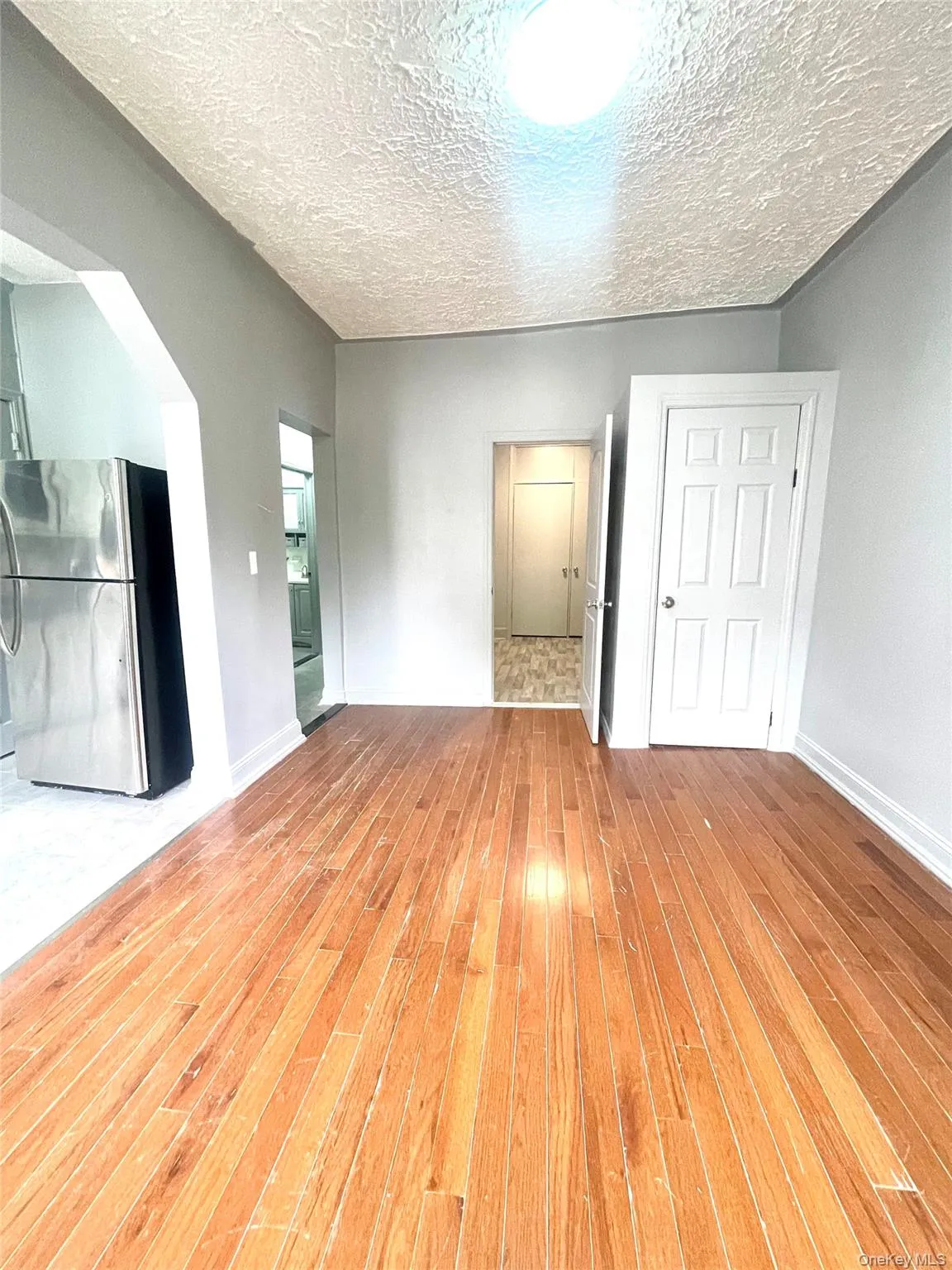 Unfurnished bedroom featuring freestanding refrigerator, a textured ceiling, light wood finished floors, arched walkways, and a closet Unfurnished bedroom featuring freestanding refrigerator, a textured ceiling, light wood finished floors, arched walkways, and a closet