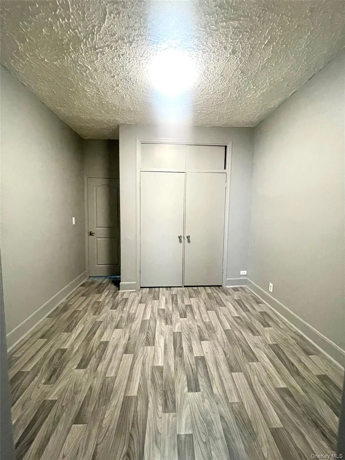 Unfurnished bedroom featuring wood finished floors, a closet, and a textured ceiling Unfurnished bedroom featuring wood finished floors, a closet, and a textured ceiling