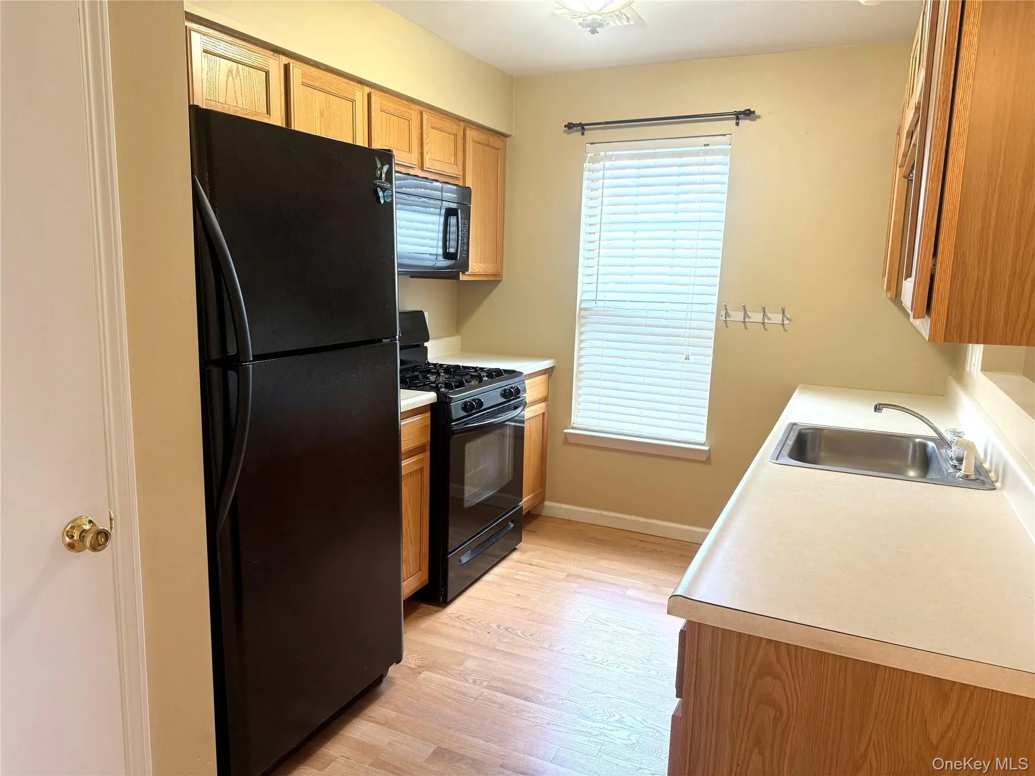 Kitchen featuring black appliances, light countertops, light wood-type flooring, and brown cabinets Kitchen featuring black appliances, light countertops, light wood-type flooring, and brown cabinets