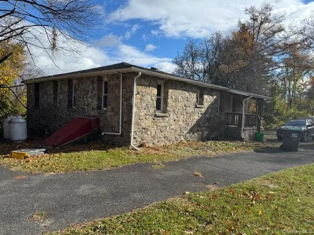 View of property side and back exterior featuring stone siding and parking area/driveway. View of property side and back exterior featuring stone siding and parking area/driveway.