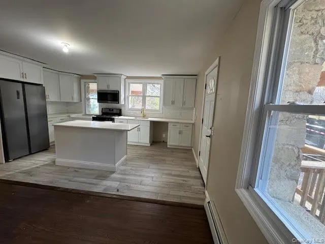 Kitchen with freestanding refrigerator, light countertops, light wood-type flooring, a baseboard heating unit, and black range with gas stovetop Kitchen with freestanding refrigerator, light countertops, light wood-type flooring, a baseboard heating unit, and black range with gas stovetop
