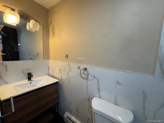 Full bath with a tub vanity, tile walls, a baseboard radiator, and wainscoting Full bath with a tub vanity, tile walls, a baseboard radiator, and wainscoting