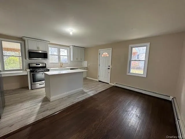 Kitchen featuring a baseboard heating unit, stainless steel appliances, light wood-style floors, and a kitchen island Kitchen featuring a baseboard heating unit, stainless steel appliances, light wood-style floors, and a kitchen island