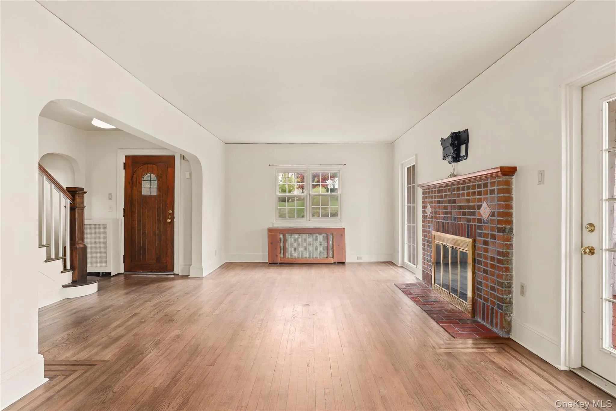 Unfurnished living room with light wood-style floors, a fireplace, stairway, and arched walkways Unfurnished living room with light wood-style floors, a fireplace, stairway, and arched walkways