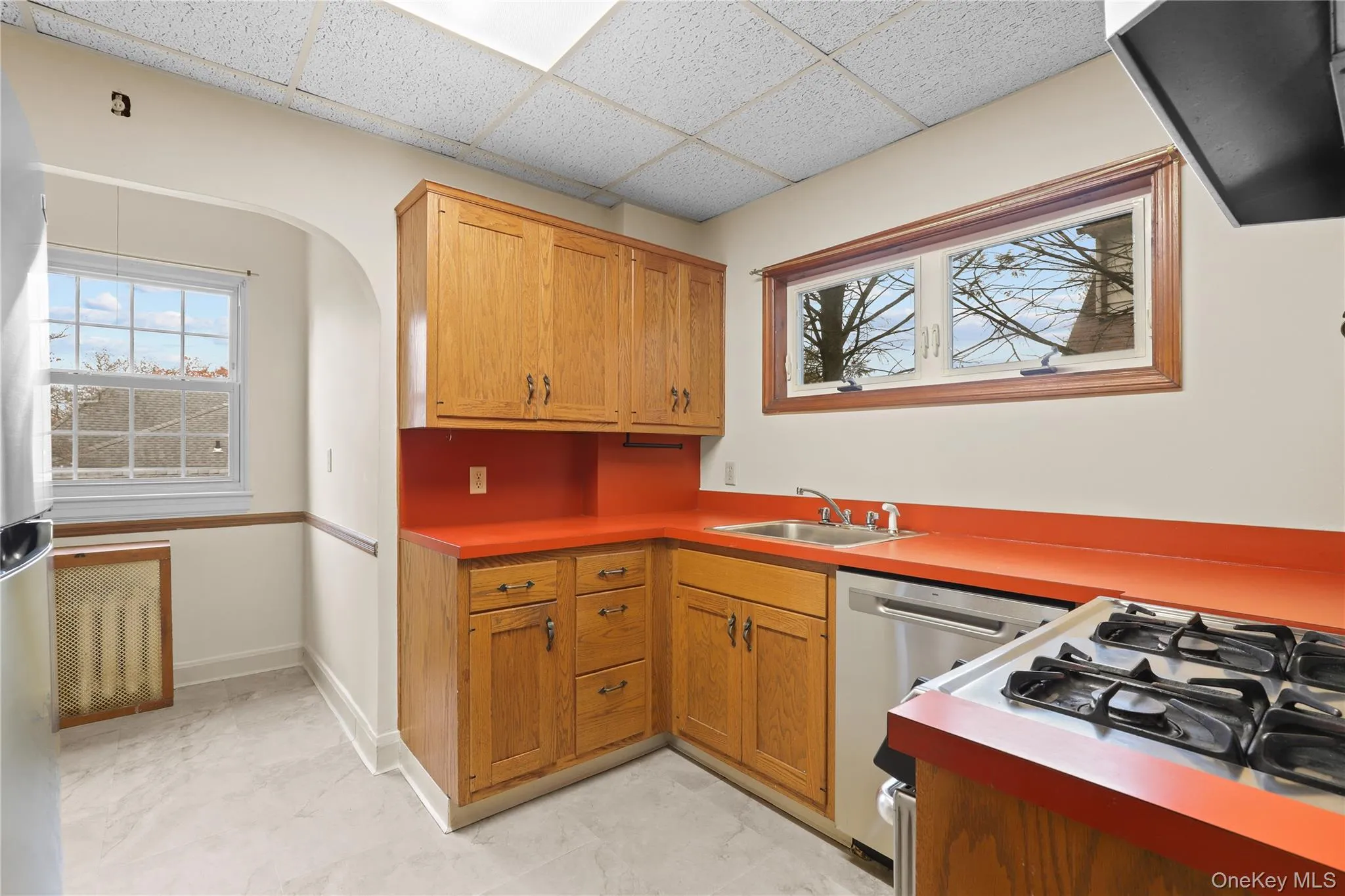 Kitchen featuring exhaust hood, stainless steel appliances, a drop ceiling, brown cabinets, and arched walkways Kitchen featuring exhaust hood, stainless steel appliances, a drop ceiling, brown cabinets, and arched walkways