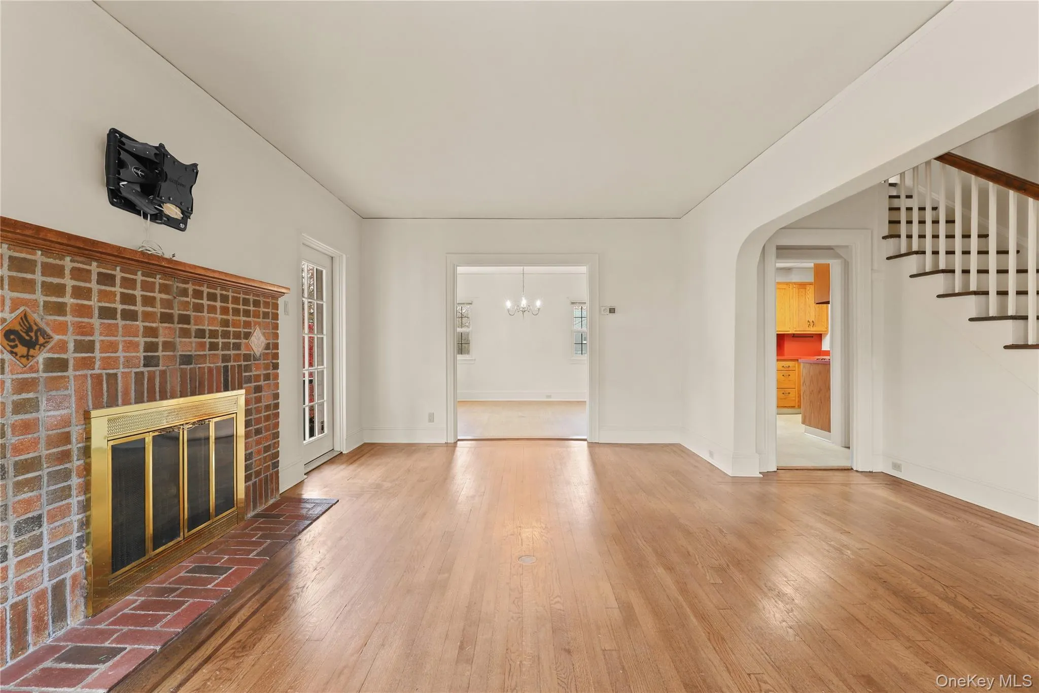 Unfurnished living room featuring wood-type flooring, a brick fireplace, stairway, and a chandelier Unfurnished living room featuring wood-type flooring, a brick fireplace, stairway, and a chandelier