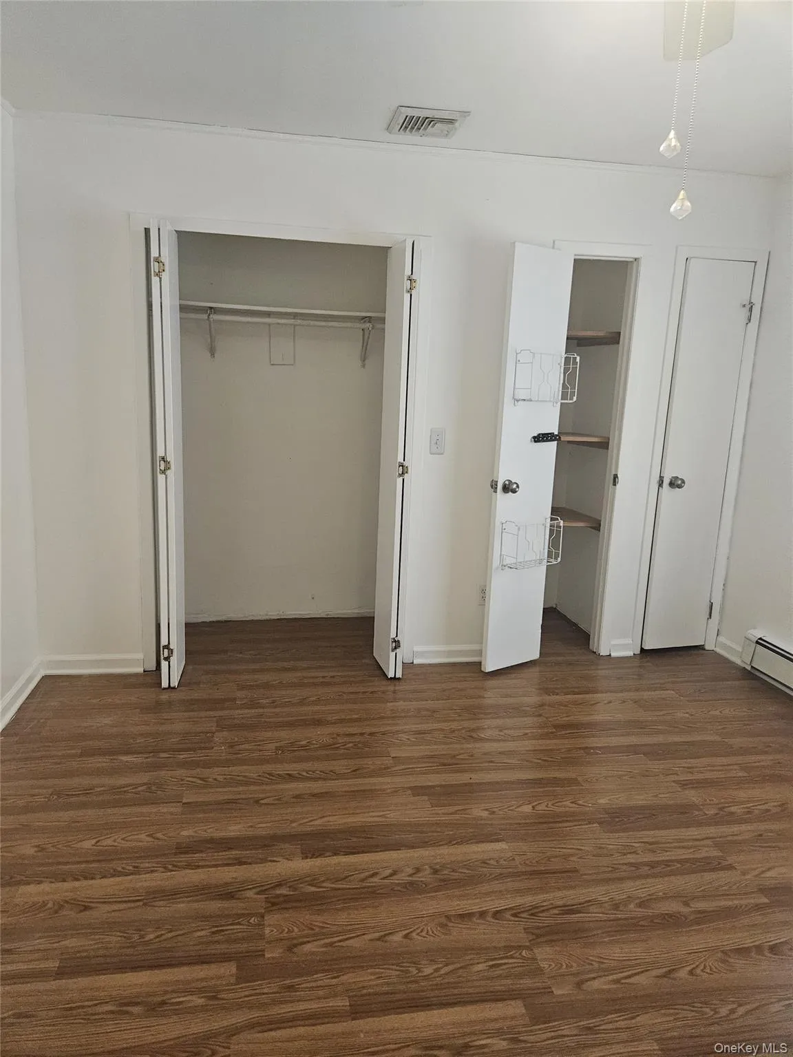Unfurnished bedroom featuring dark wood-style flooring, a closet, and baseboard heating Unfurnished bedroom featuring dark wood-style flooring, a closet, and baseboard heating
