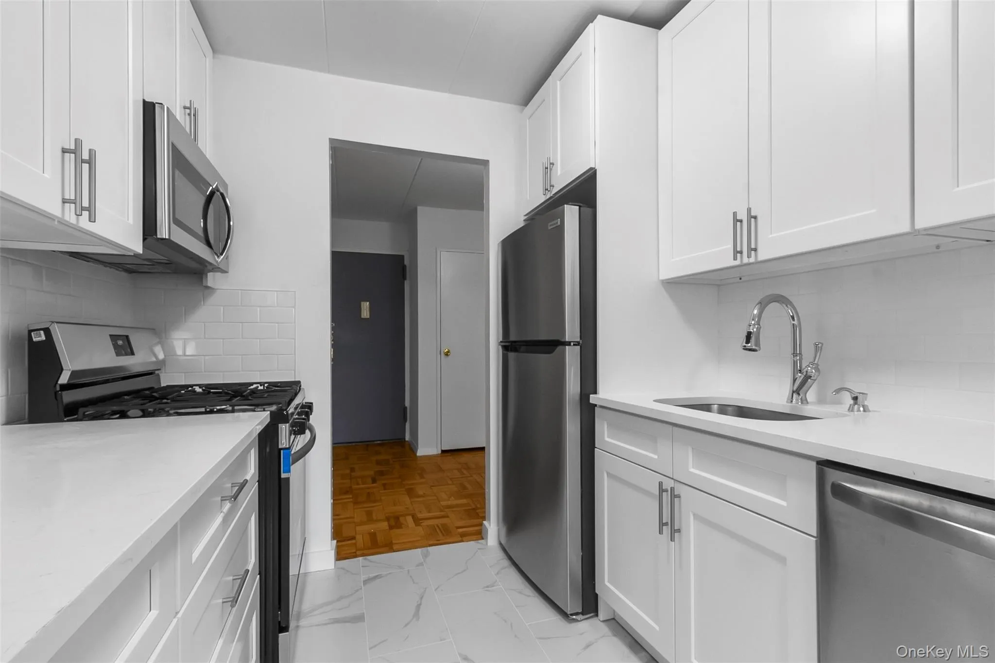 Kitchen with decorative backsplash, appliances with stainless steel finishes, white cabinetry, and light stone counters Kitchen with decorative backsplash, appliances with stainless steel finishes, white cabinetry, and light stone counters