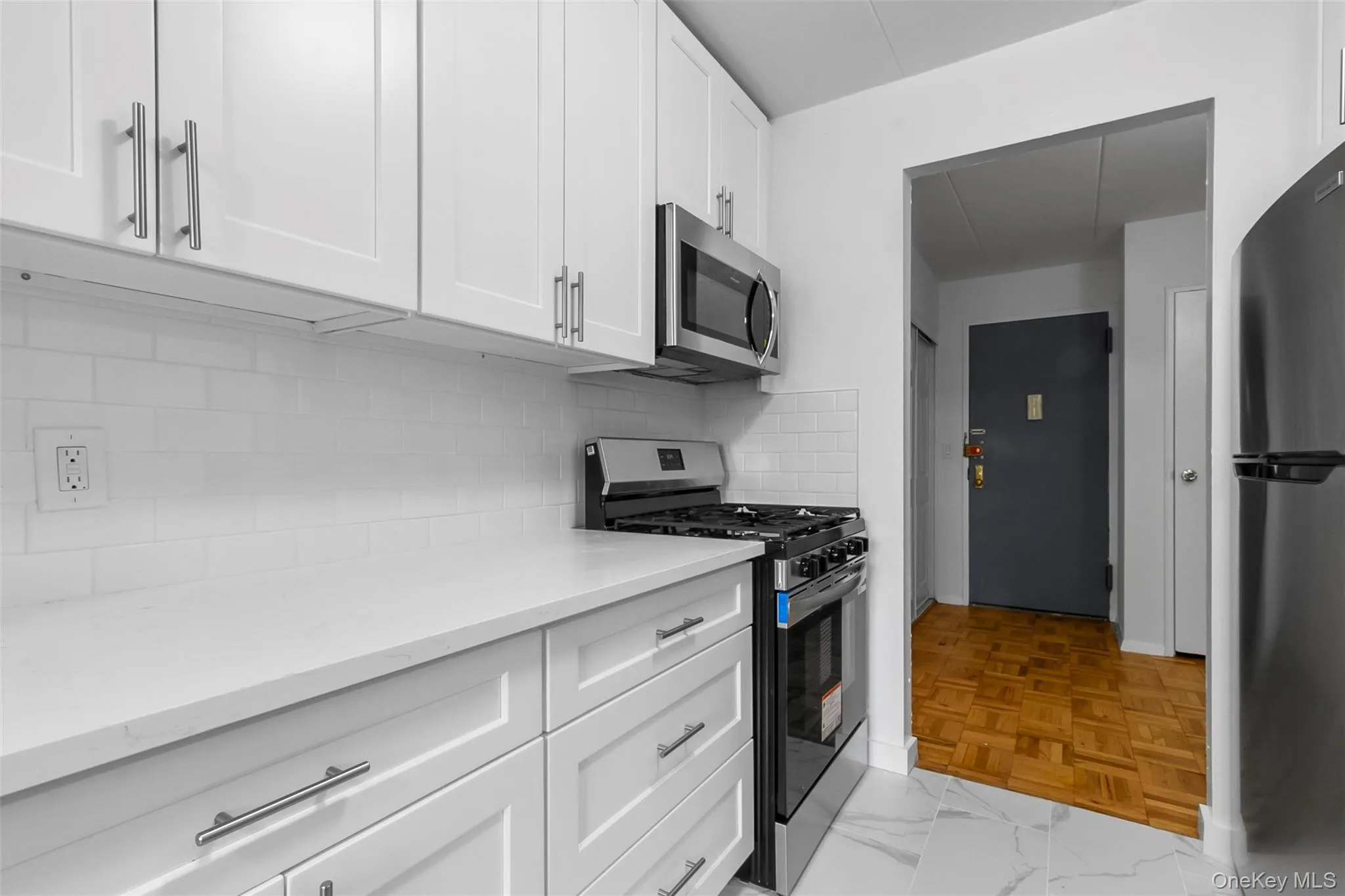 Kitchen featuring stainless steel appliances, white cabinetry, tasteful backsplash, light stone countertops, and light marble finish flooring Kitchen featuring stainless steel appliances, white cabinetry, tasteful backsplash, light stone countertops, and light marble finish flooring