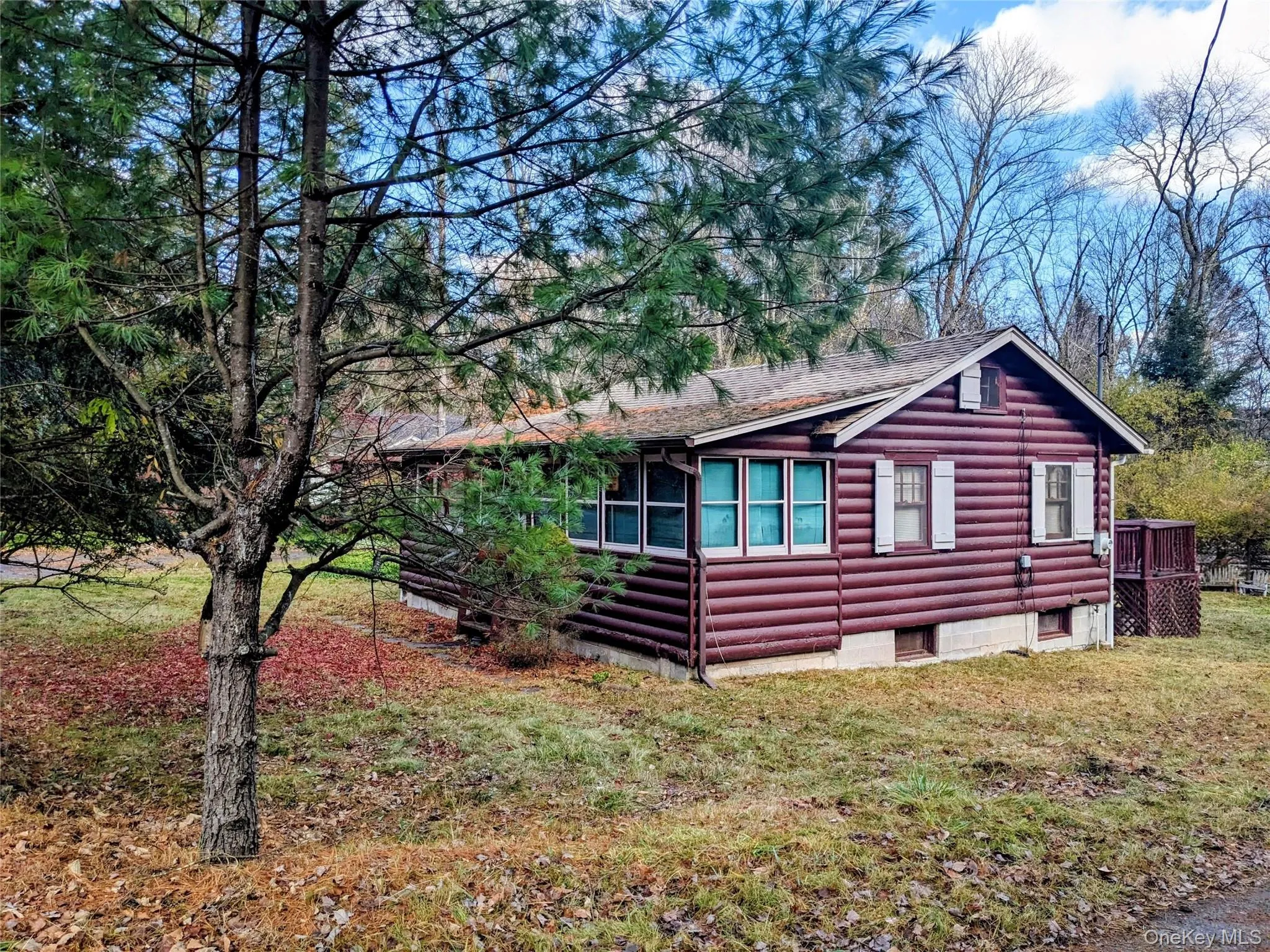 View of property exterior featuring a yard, a shingled roof, a wooden deck, and log veneer siding View of property exterior featuring a yard, a shingled roof, a wooden deck, and log veneer siding
