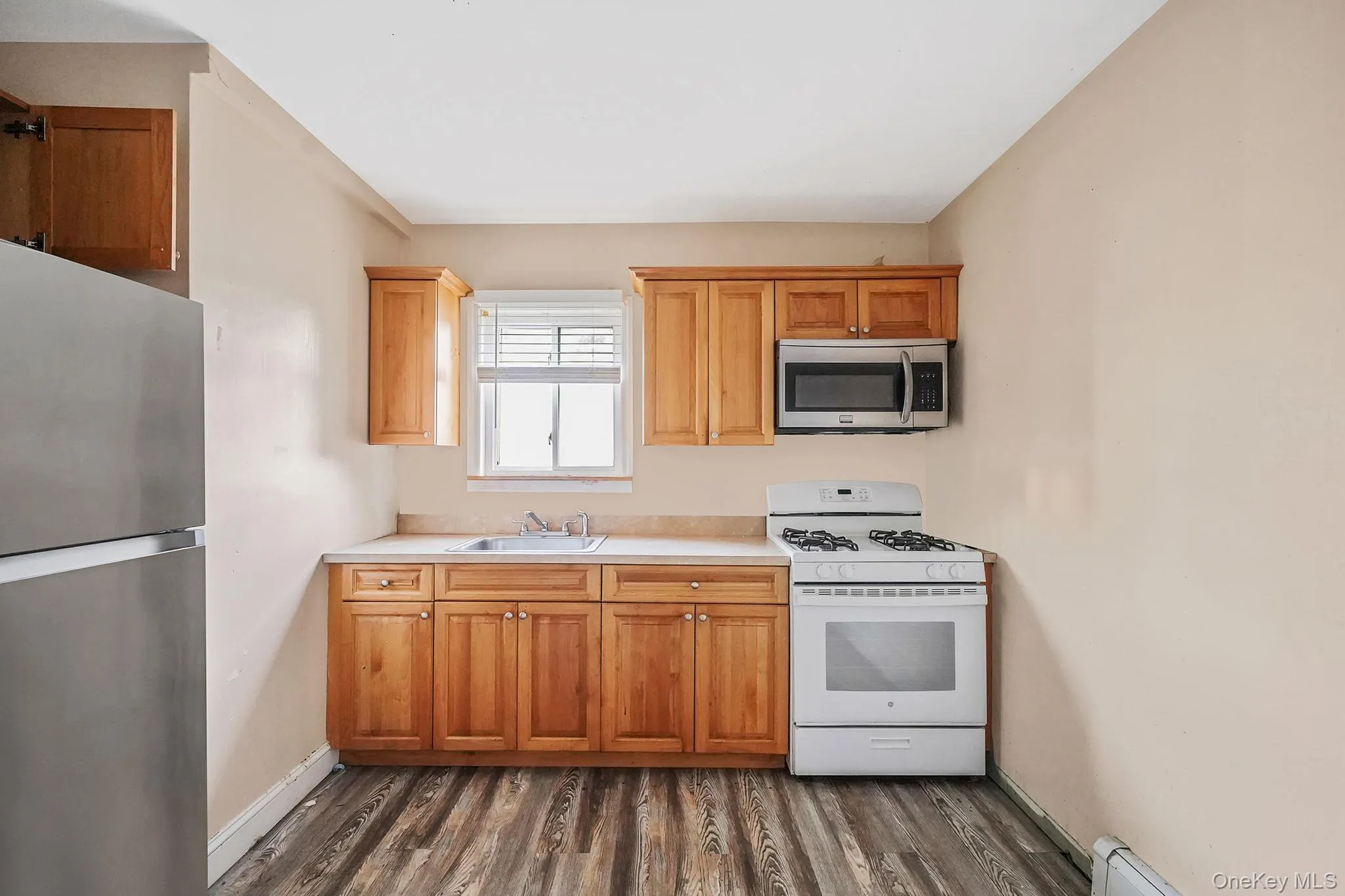 Kitchen featuring appliances with stainless steel finishes, light countertops, dark wood-style floors, a baseboard radiator, and brown cabinetry Kitchen featuring appliances with stainless steel finishes, light countertops, dark wood-style floors, a baseboard radiator, and brown cabinetry