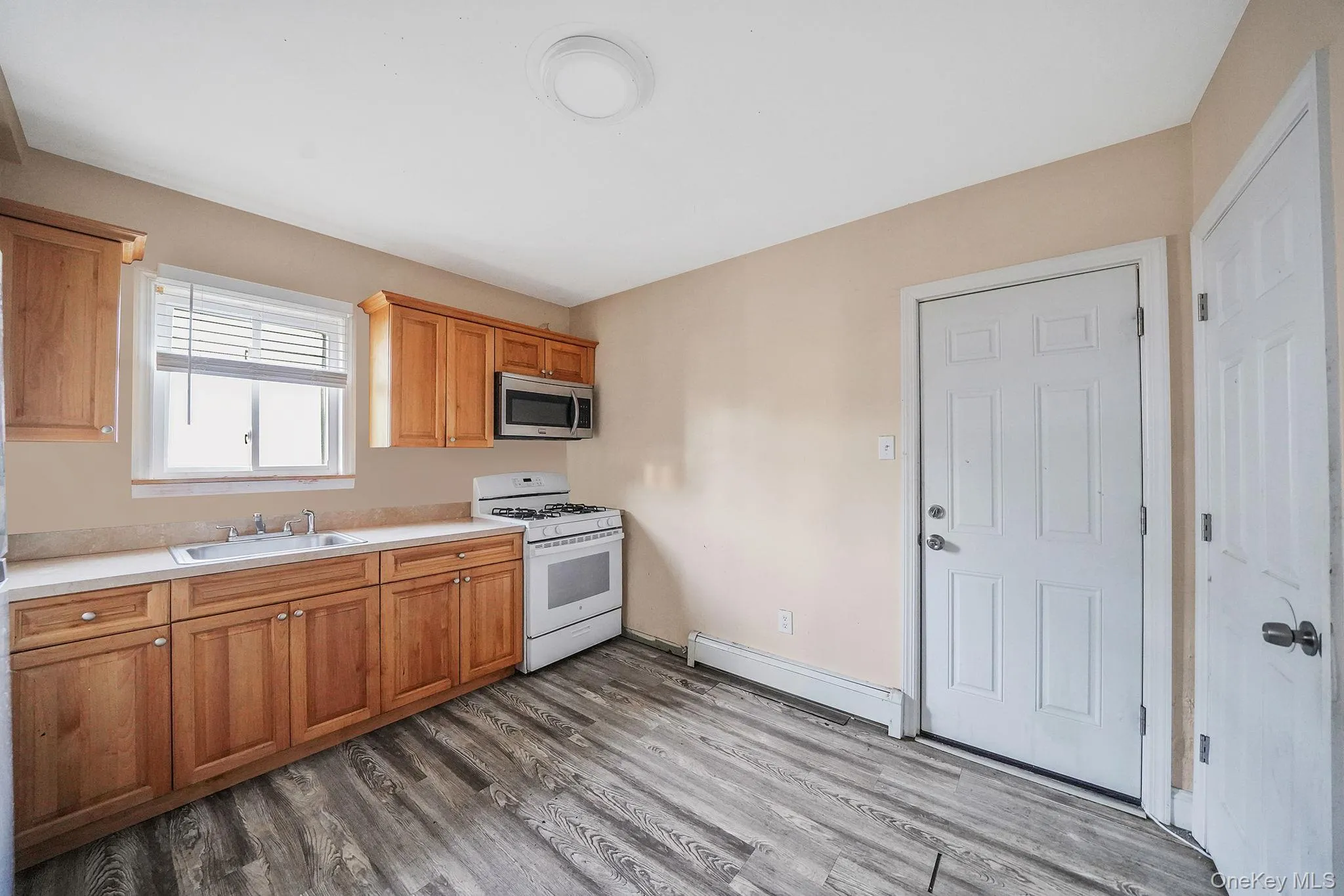 Kitchen featuring gas range gas stove, light countertops, stainless steel microwave, dark wood-type flooring, and baseboard heating Kitchen featuring gas range gas stove, light countertops, stainless steel microwave, dark wood-type flooring, and baseboard heating