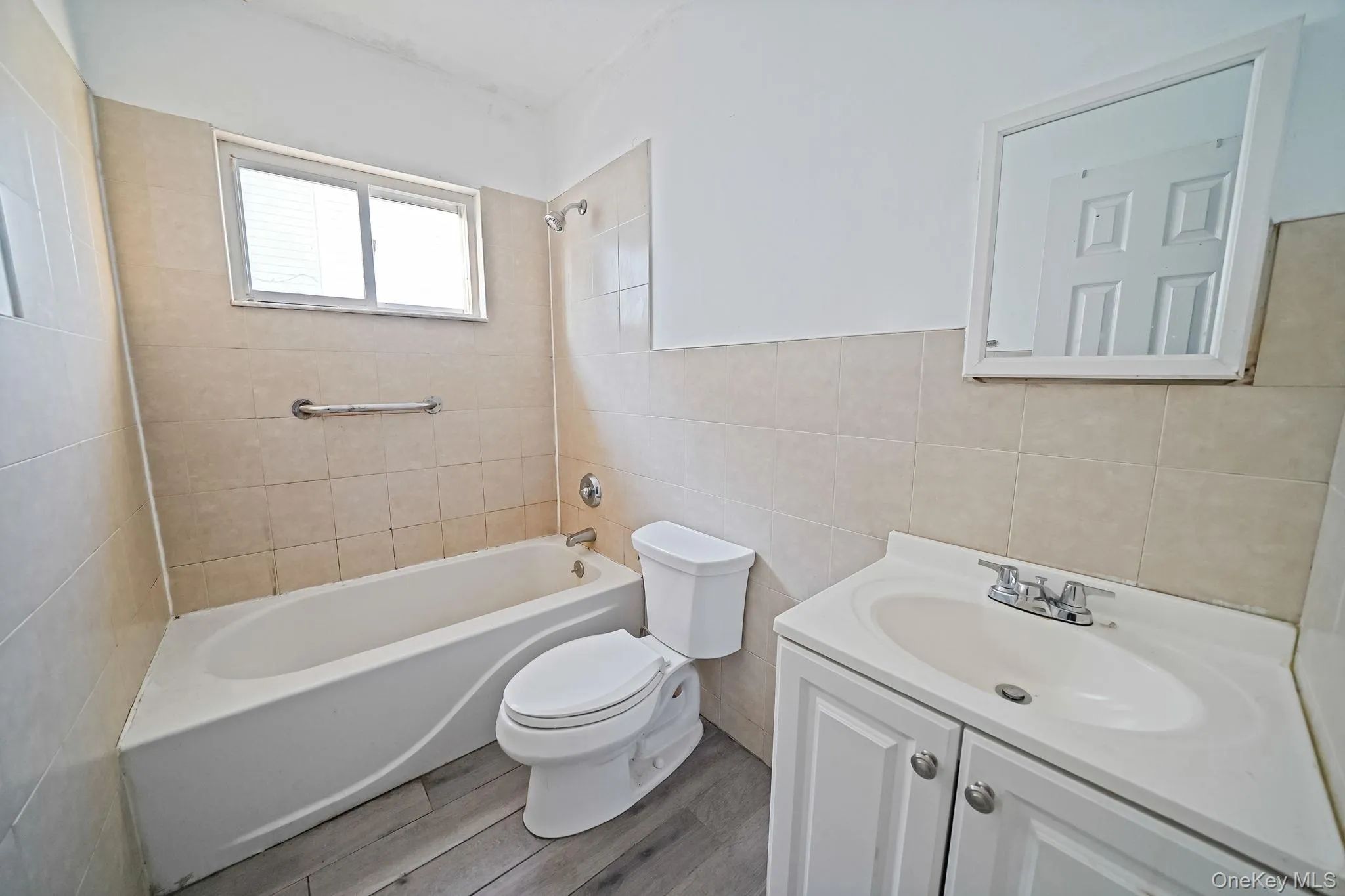 Bathroom featuring shower / tub combination, vanity, wood finished floors, and tile walls Bathroom featuring shower / tub combination, vanity, wood finished floors, and tile walls