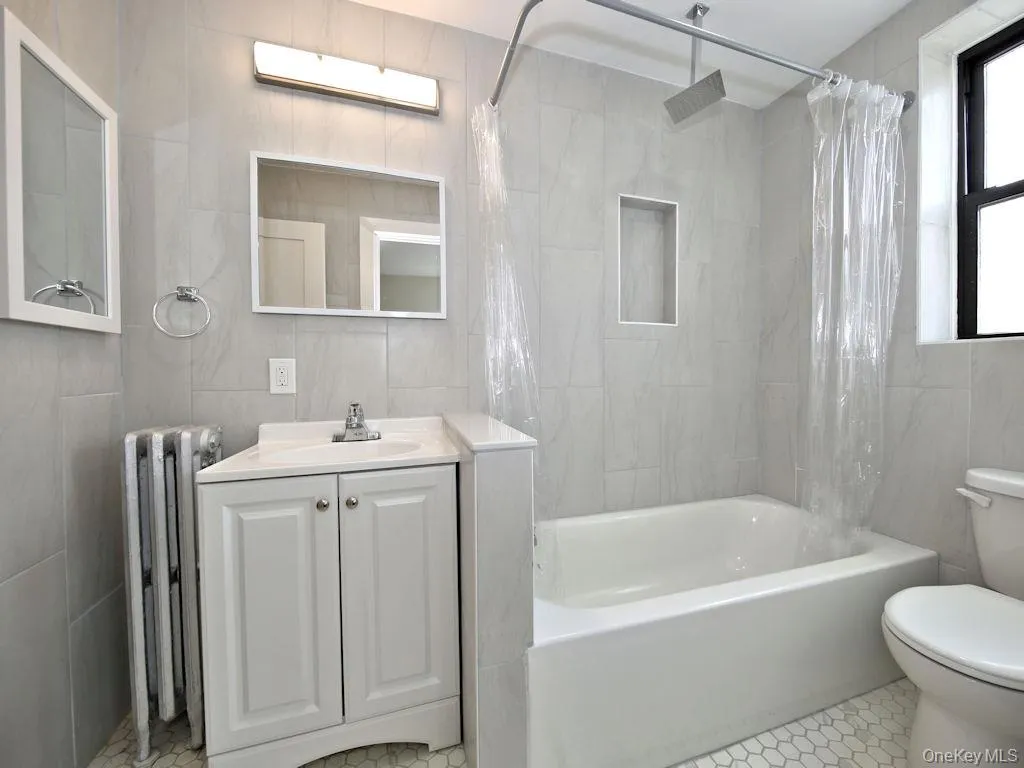 Bathroom featuring tile walls, a combined bath / shower with rainfall shower, radiator heating unit, and vanity Bathroom featuring tile walls, a combined bath / shower with rainfall shower, radiator heating unit, and vanity