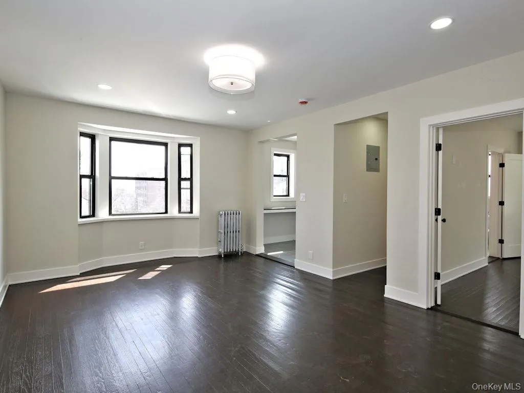 Empty room featuring radiator, recessed lighting, dark wood-style flooring, and electric panel Empty room featuring radiator, recessed lighting, dark wood-style flooring, and electric panel