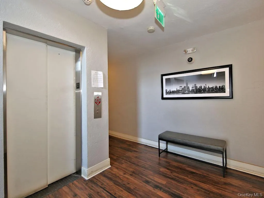 Hallway featuring elevator, dark wood-type flooring, and a textured wall Hallway featuring elevator, dark wood-type flooring, and a textured wall