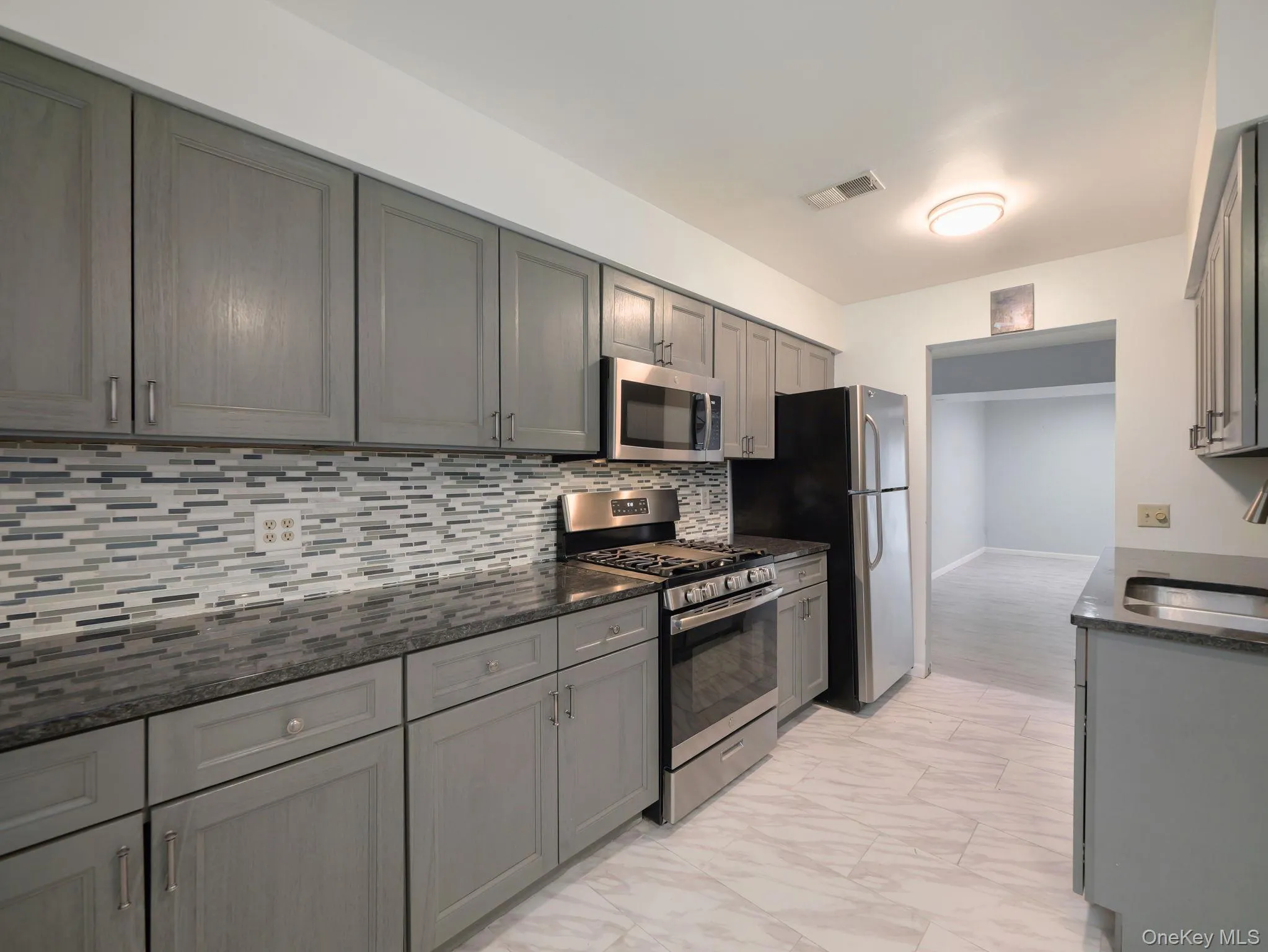 Kitchen featuring stainless steel appliances, gray cabinetry, decorative backsplash, and light marble finish floors Kitchen featuring stainless steel appliances, gray cabinetry, decorative backsplash, and light marble finish floors