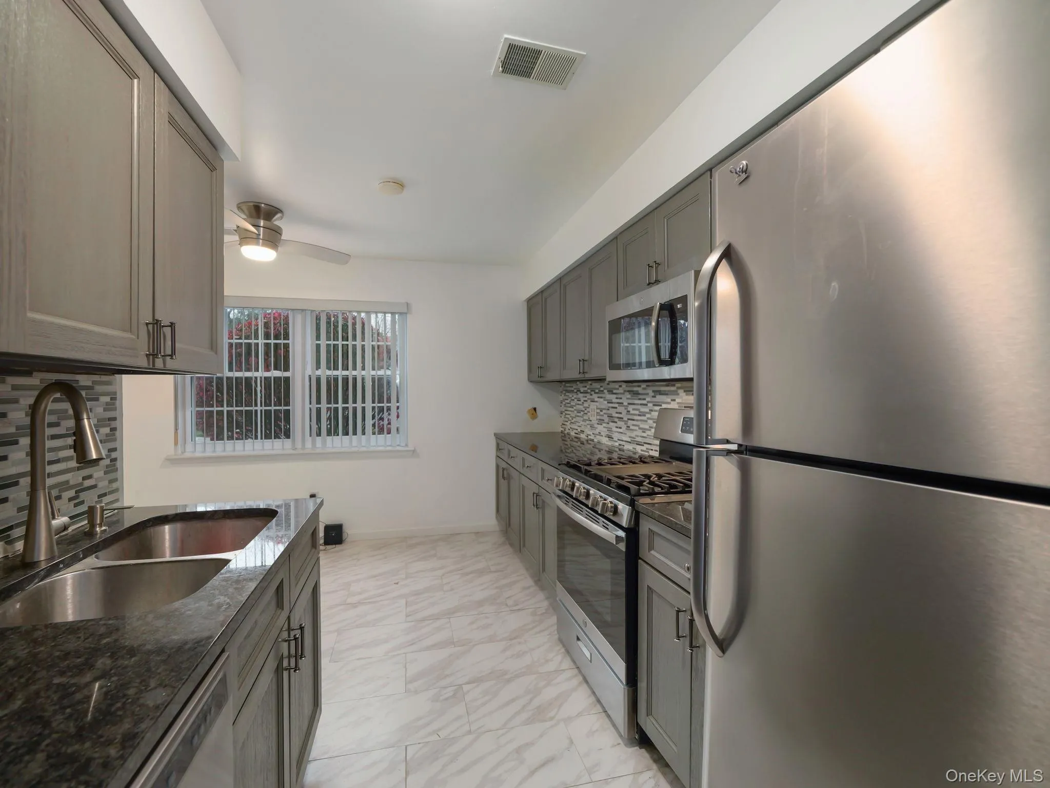 Kitchen with stainless steel appliances, decorative backsplash, dark stone countertops, gray cabinets, and a ceiling fan Kitchen with stainless steel appliances, decorative backsplash, dark stone countertops, gray cabinets, and a ceiling fan