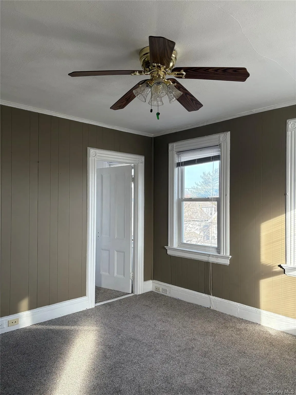Carpeted spare room with crown molding, ceiling fan, and wooden walls Carpeted spare room with crown molding, ceiling fan, and wooden walls