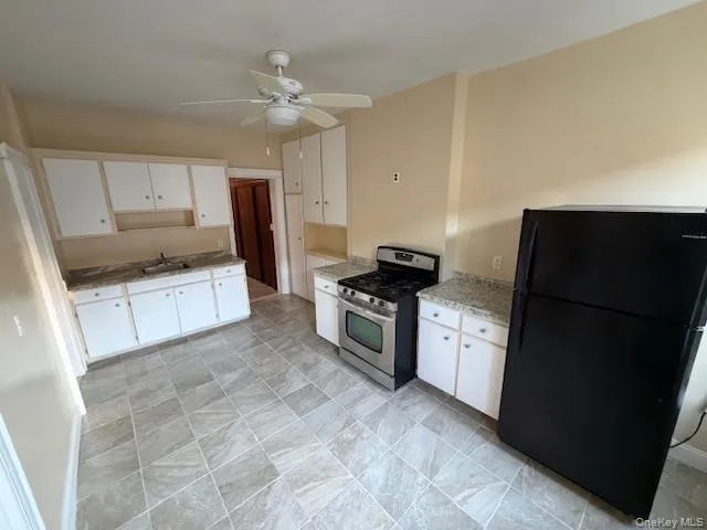 Kitchen featuring freestanding refrigerator, stainless steel gas stove, white cabinets, ceiling fan, and light stone counters Kitchen featuring freestanding refrigerator, stainless steel gas stove, white cabinets, ceiling fan, and light stone counters