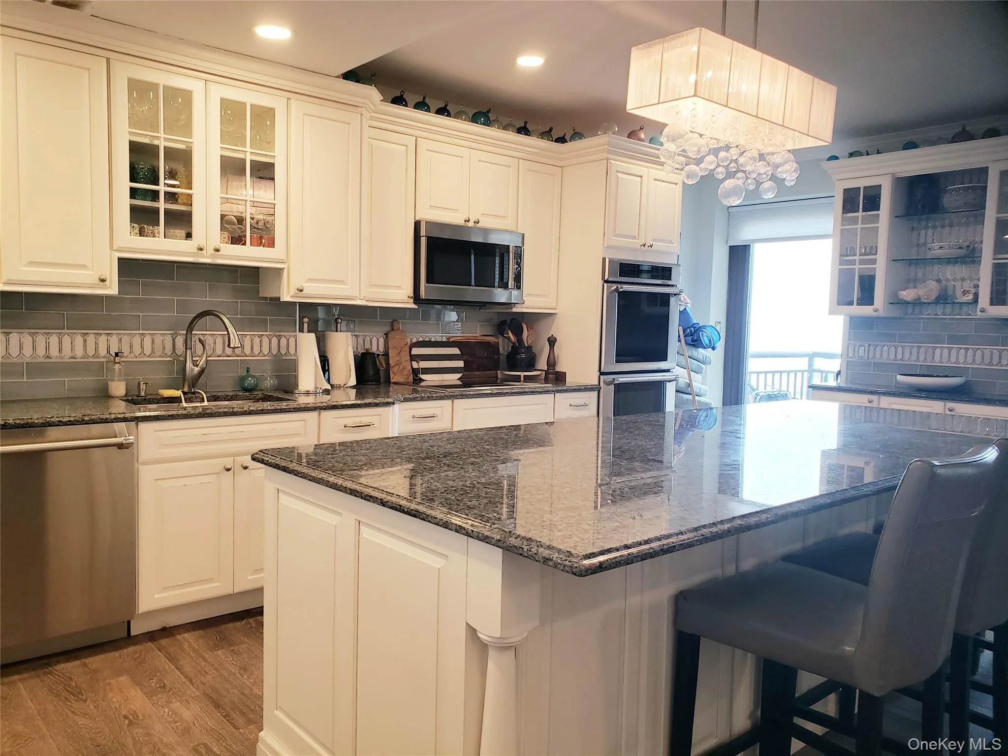 Kitchen featuring light wood-type flooring, decorative backsplash, a kitchen island, a sink, and appliances with stainless steel finishes Kitchen featuring light wood-type flooring, decorative backsplash, a kitchen island, a sink, and appliances with stainless steel finishes