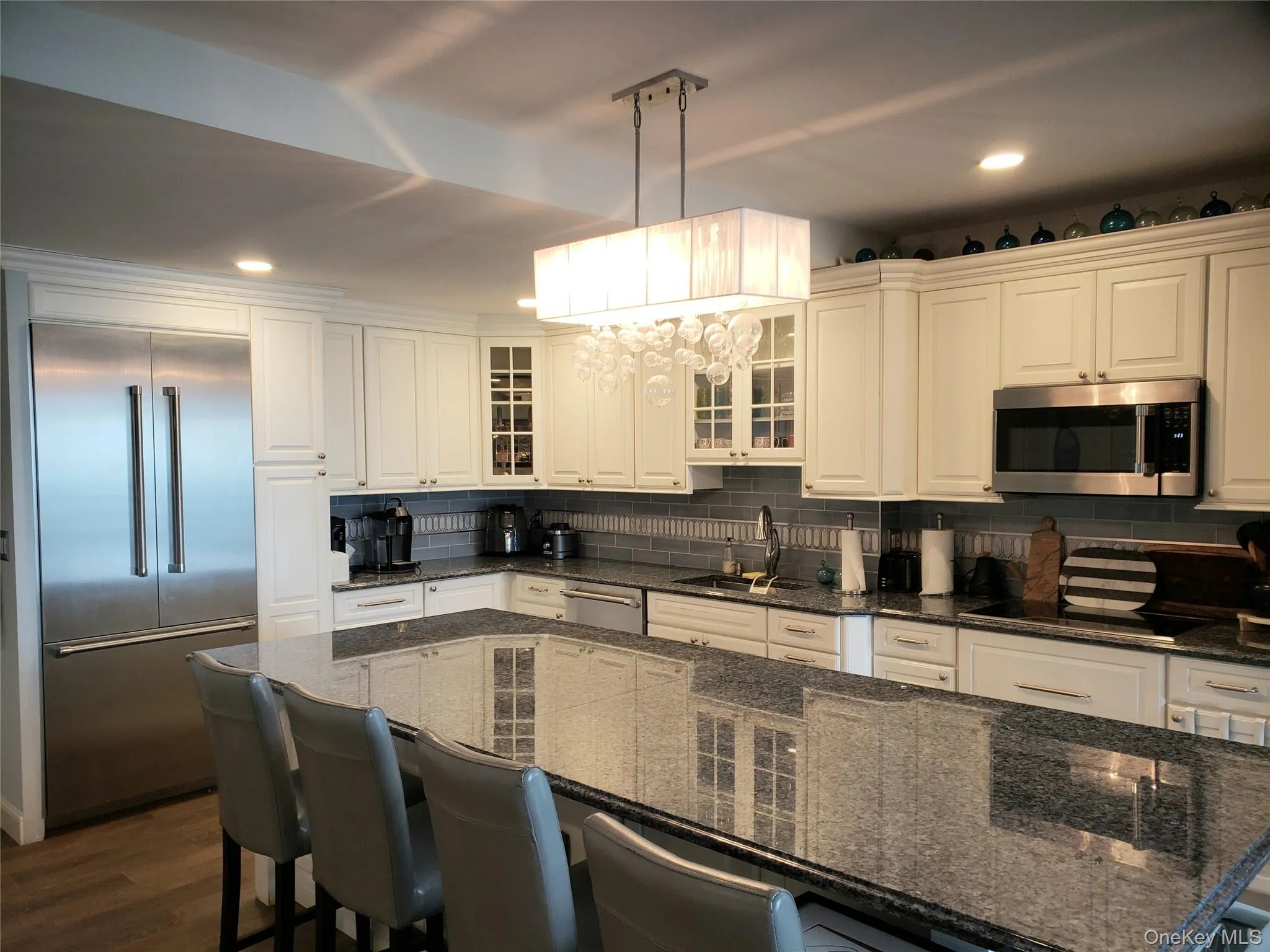 Kitchen with a sink, a chandelier, appliances with stainless steel finishes, glass insert cabinets, and decorative backsplash Kitchen with a sink, a chandelier, appliances with stainless steel finishes, glass insert cabinets, and decorative backsplash
