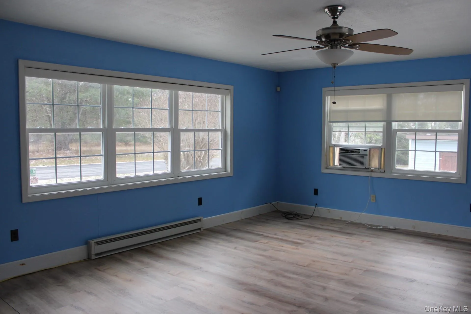 Empty room with a baseboard radiator, light wood finished floors, and a ceiling fan Empty room with a baseboard radiator, light wood finished floors, and a ceiling fan