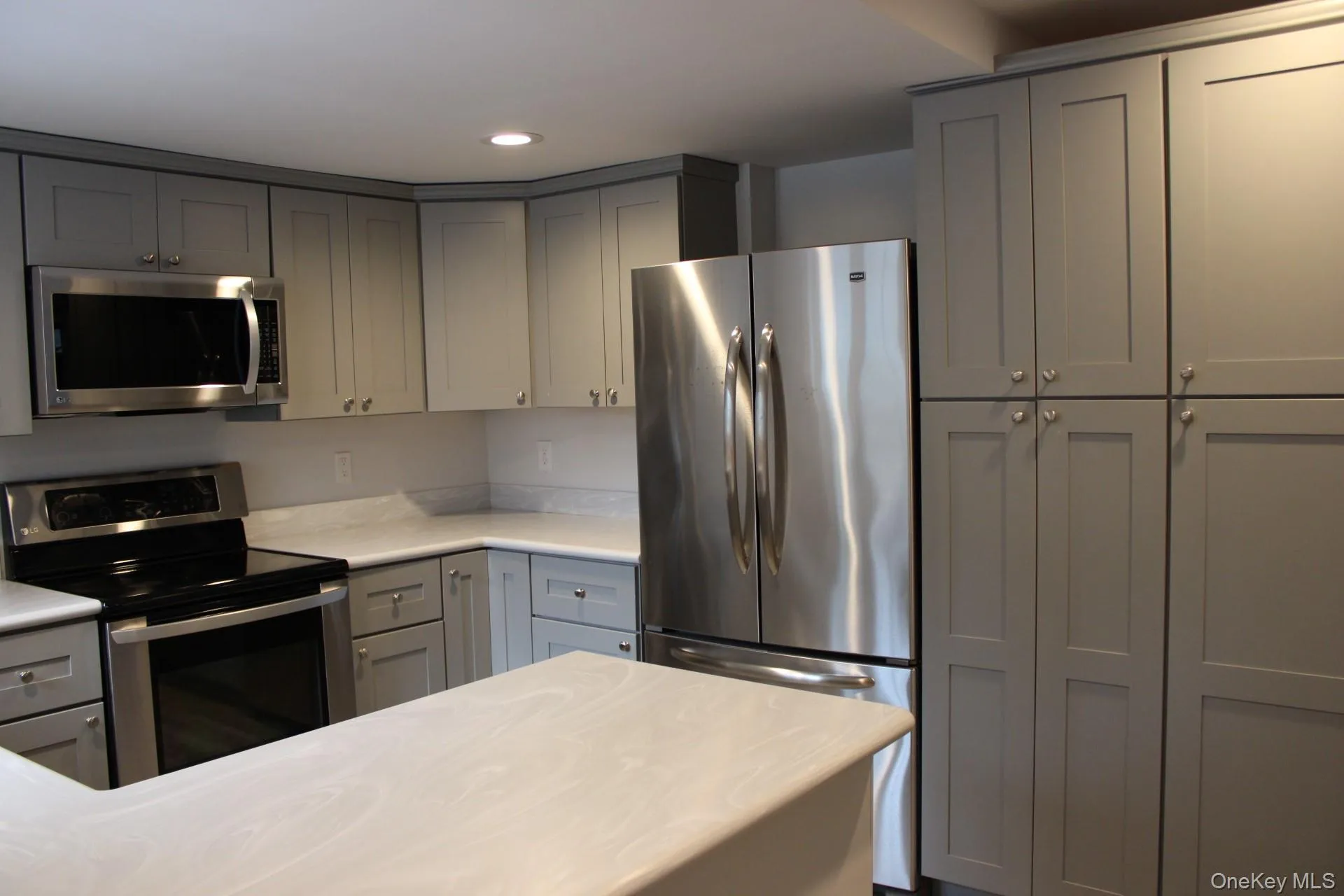 Kitchen with gray cabinets, stainless steel appliances, recessed lighting, and light stone counters Kitchen with gray cabinets, stainless steel appliances, recessed lighting, and light stone counters