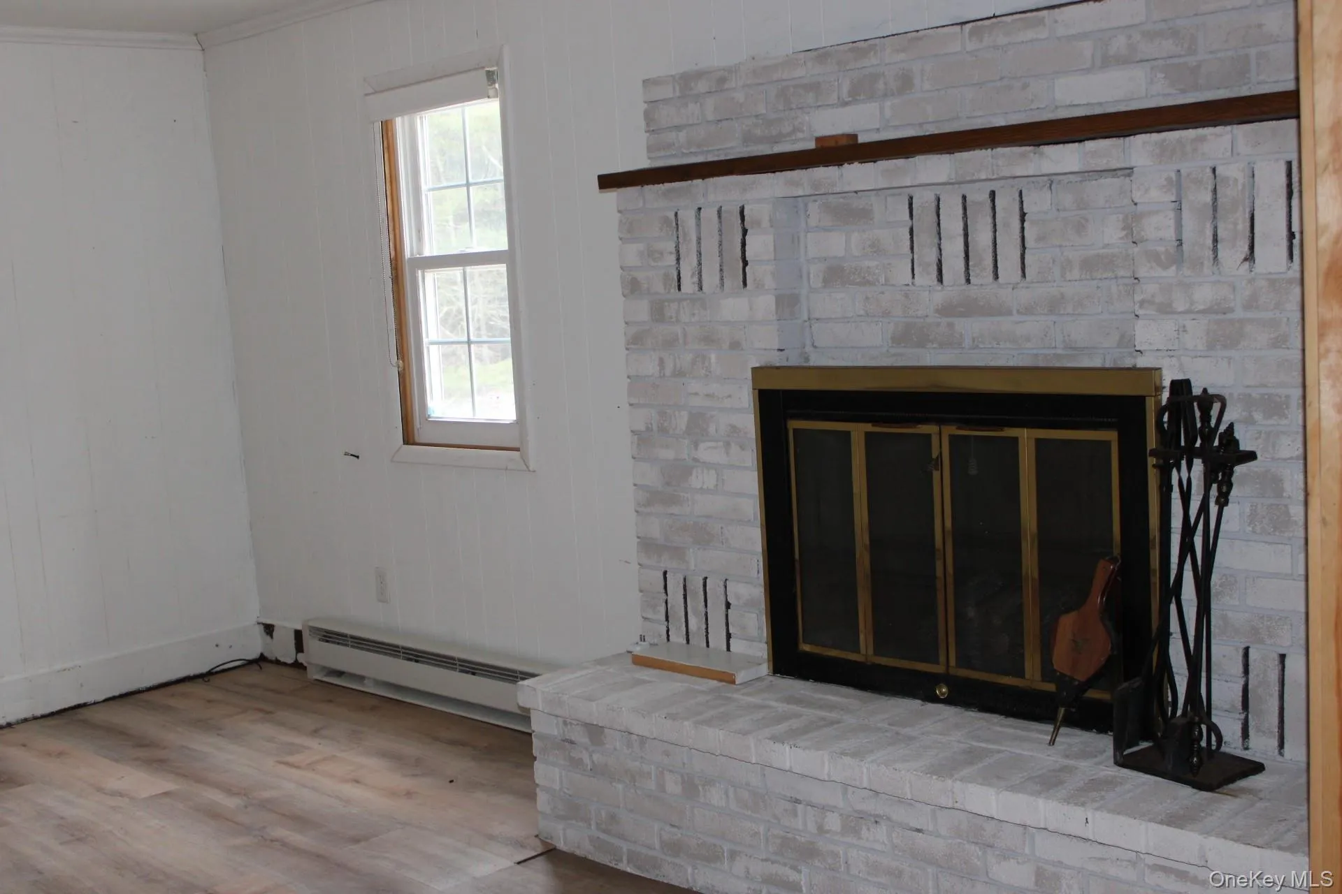 Detailed view of wood finished floors, baseboard heating, a brick fireplace, and wooden walls Detailed view of wood finished floors, baseboard heating, a brick fireplace, and wooden walls
