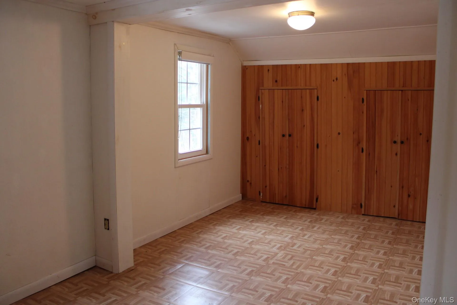 Unfurnished bedroom with wooden walls, vaulted ceiling, and a closet Unfurnished bedroom with wooden walls, vaulted ceiling, and a closet