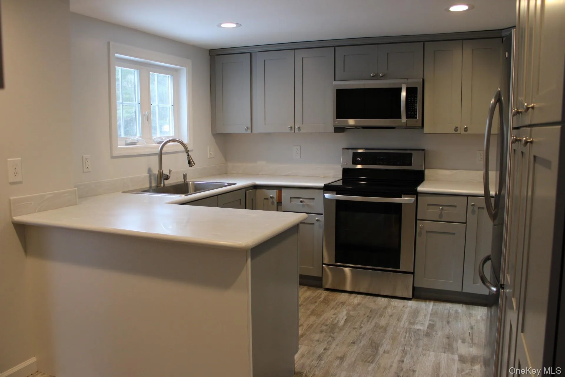Kitchen with gray cabinetry, stainless steel appliances, a peninsula, light countertops, and recessed lighting Kitchen with gray cabinetry, stainless steel appliances, a peninsula, light countertops, and recessed lighting