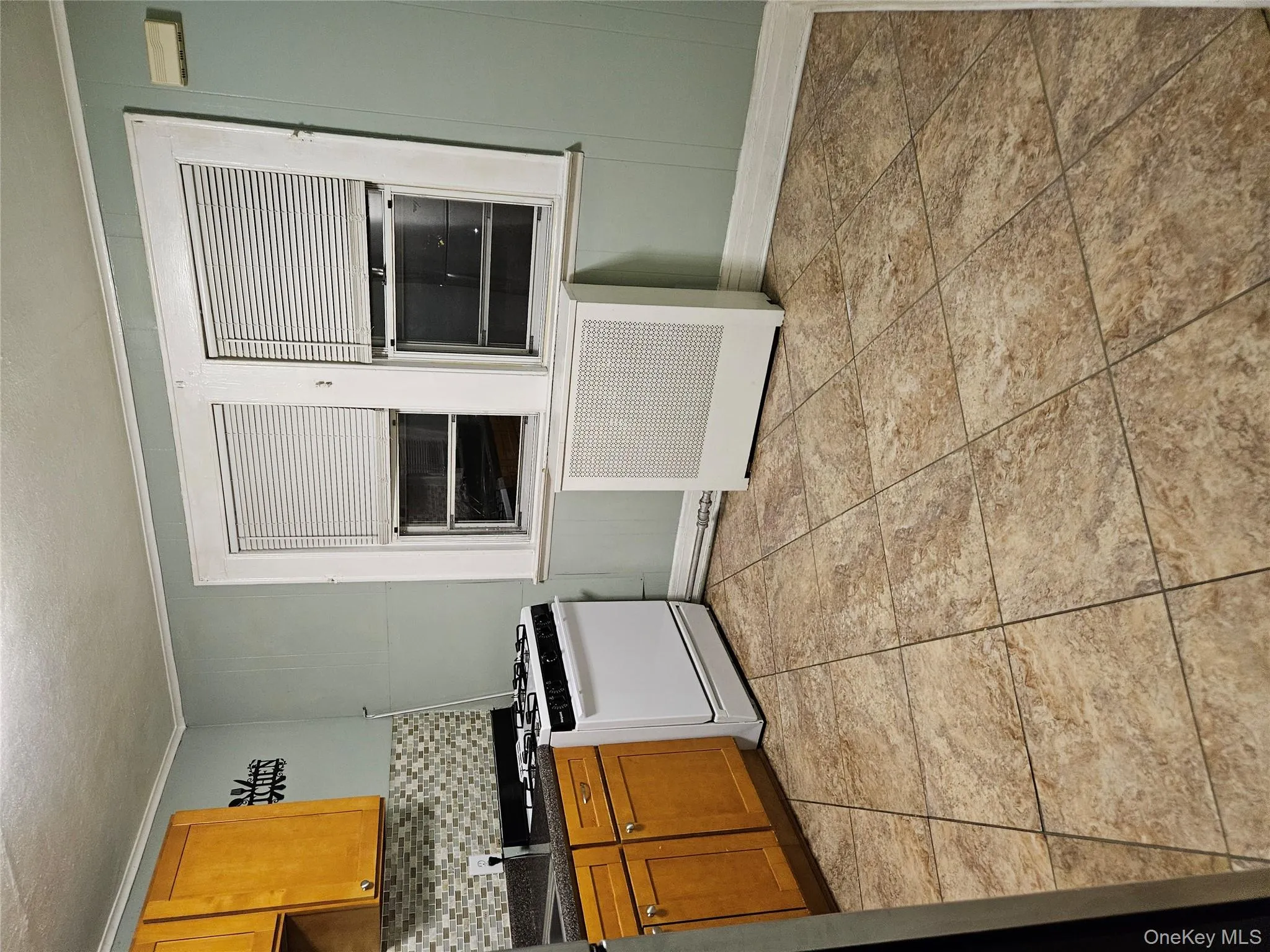 Kitchen with dark countertops, range, decorative backsplash, brown cabinetry, and radiator Kitchen with dark countertops, range, decorative backsplash, brown cabinetry, and radiator