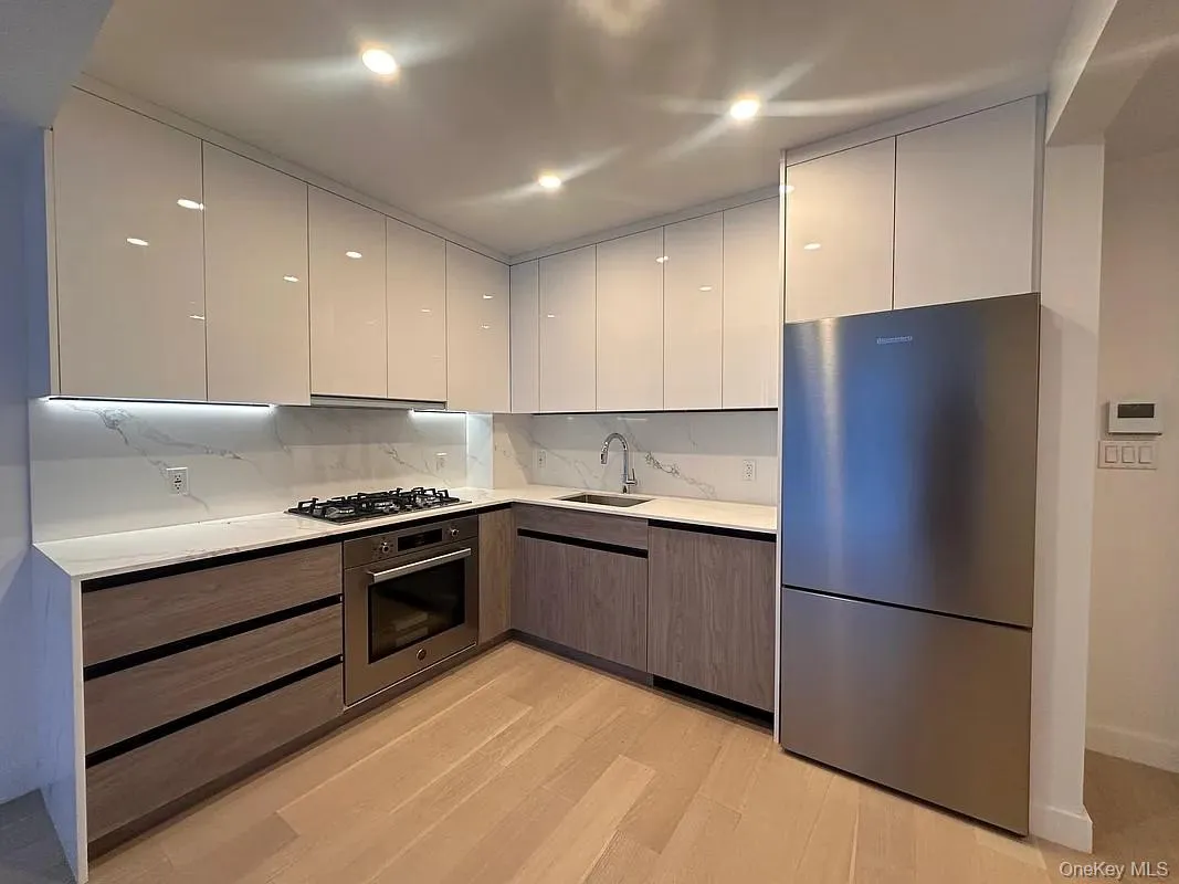 Kitchen with modern cabinets, appliances with stainless steel finishes, white cabinets, light wood finished floors, and tasteful backsplash Kitchen with modern cabinets, appliances with stainless steel finishes, white cabinets, light wood finished floors, and tasteful backsplash