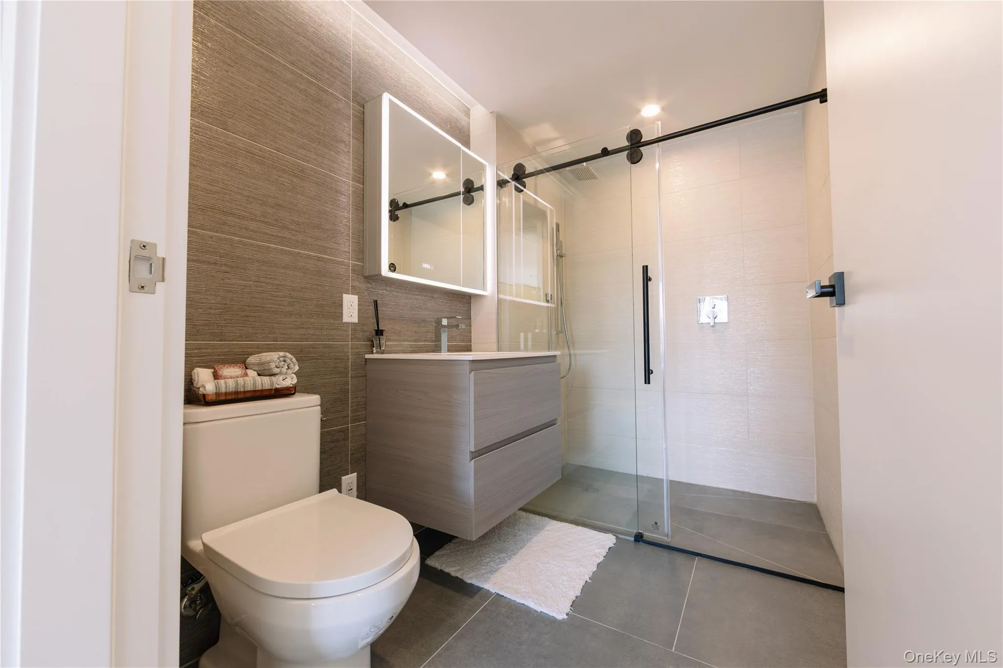 Bathroom with vanity, a stall shower, dark tile patterned floors, and tile walls Bathroom with vanity, a stall shower, dark tile patterned floors, and tile walls