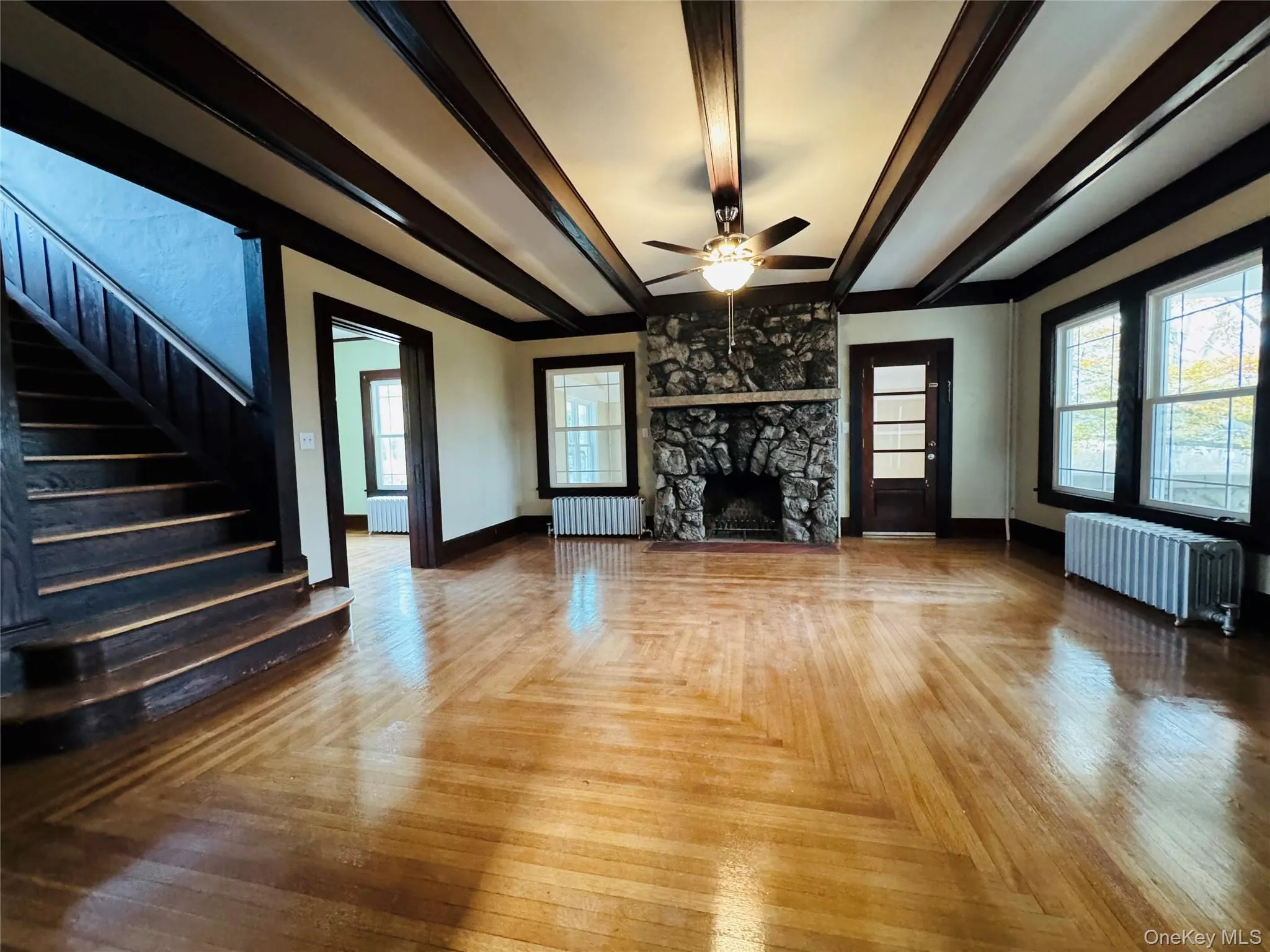Unfurnished living room featuring beamed ceiling, radiator heating unit, plenty of natural light, and ceiling fan Unfurnished living room featuring beamed ceiling, radiator heating unit, plenty of natural light, and ceiling fan