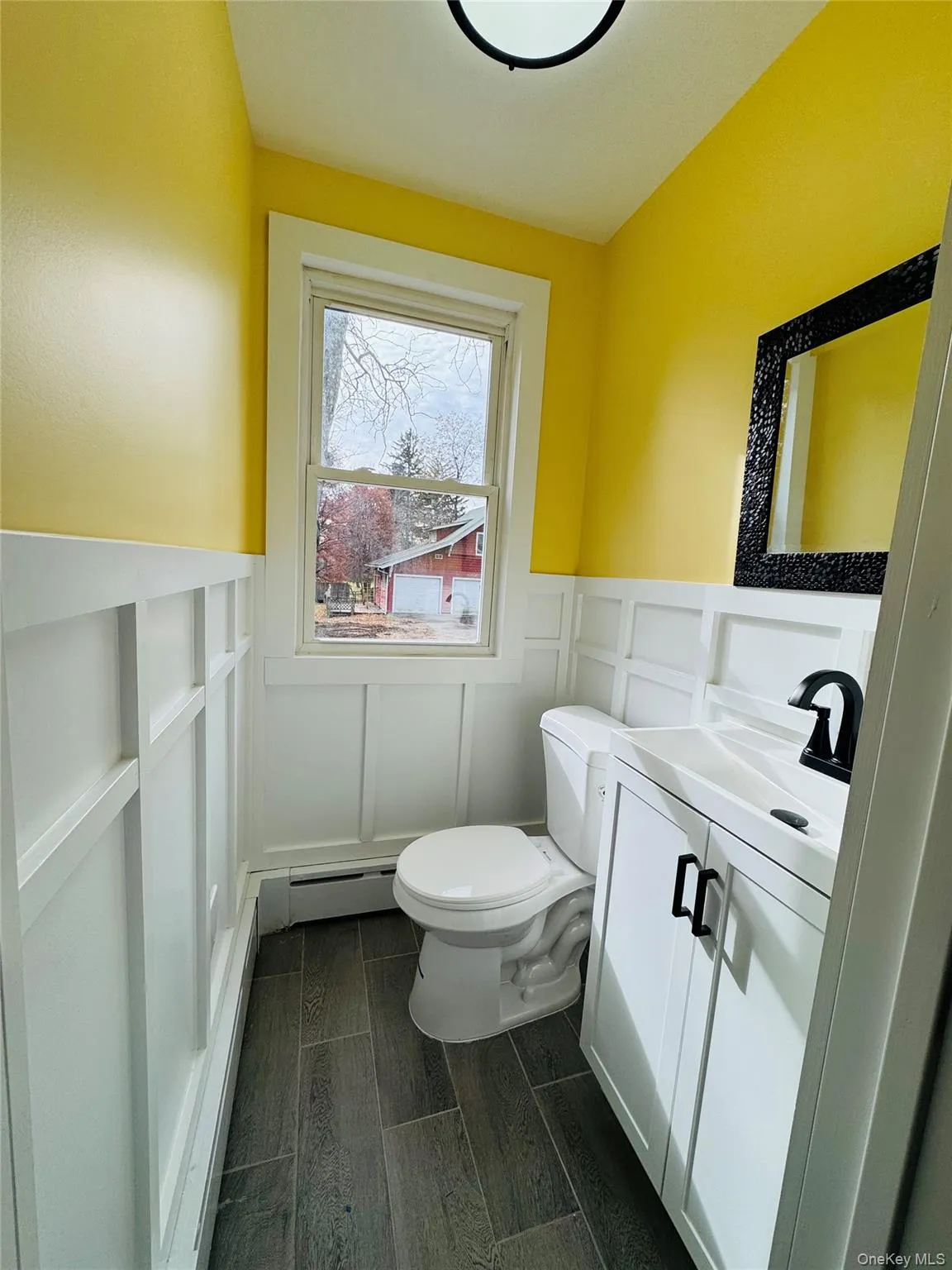 Half bathroom with vanity, a decorative wall, wood finish floors, a wainscoted wall, and a baseboard heating unit Half bathroom with vanity, a decorative wall, wood finish floors, a wainscoted wall, and a baseboard heating unit