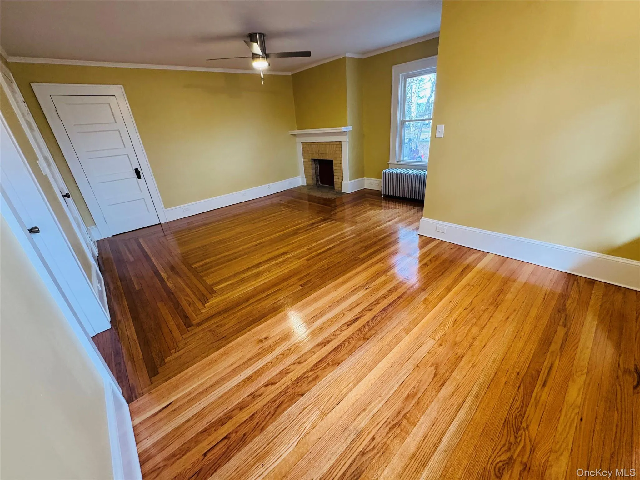 Unfurnished living room with ornamental molding, radiator heating unit, a fireplace, wood finished floors, and ceiling fan Unfurnished living room with ornamental molding, radiator heating unit, a fireplace, wood finished floors, and ceiling fan