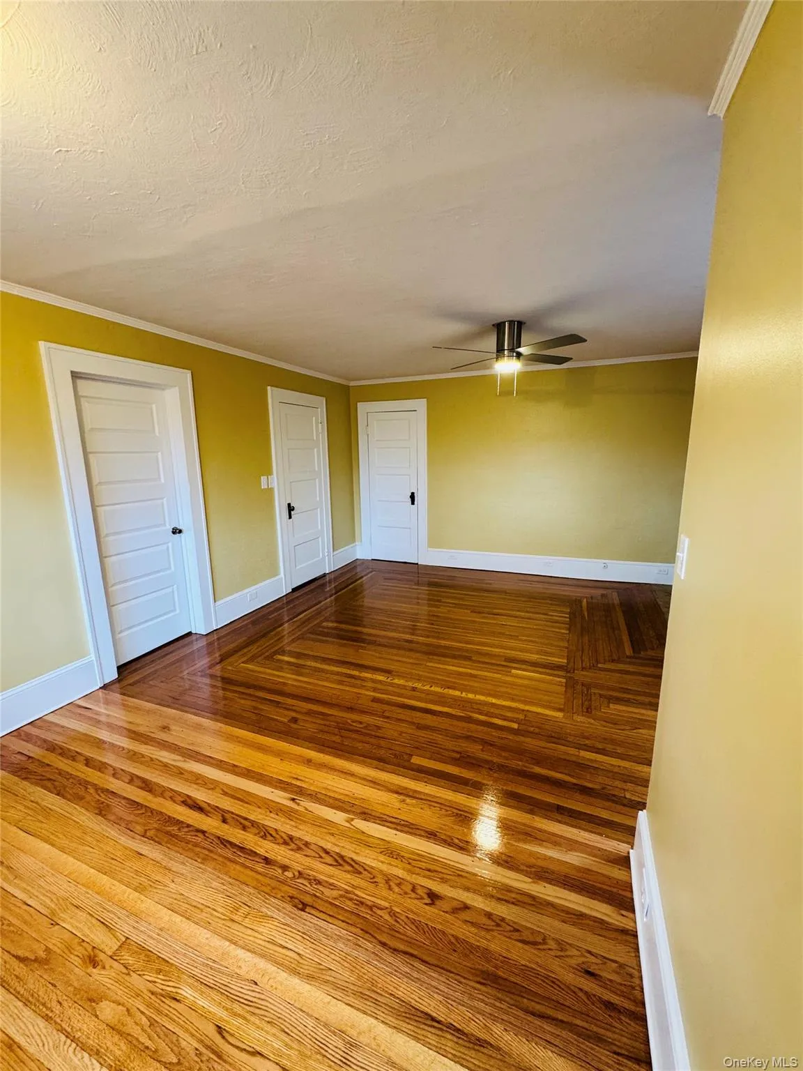 Empty room with wood-type flooring, crown molding, a textured ceiling, and ceiling fan Empty room with wood-type flooring, crown molding, a textured ceiling, and ceiling fan