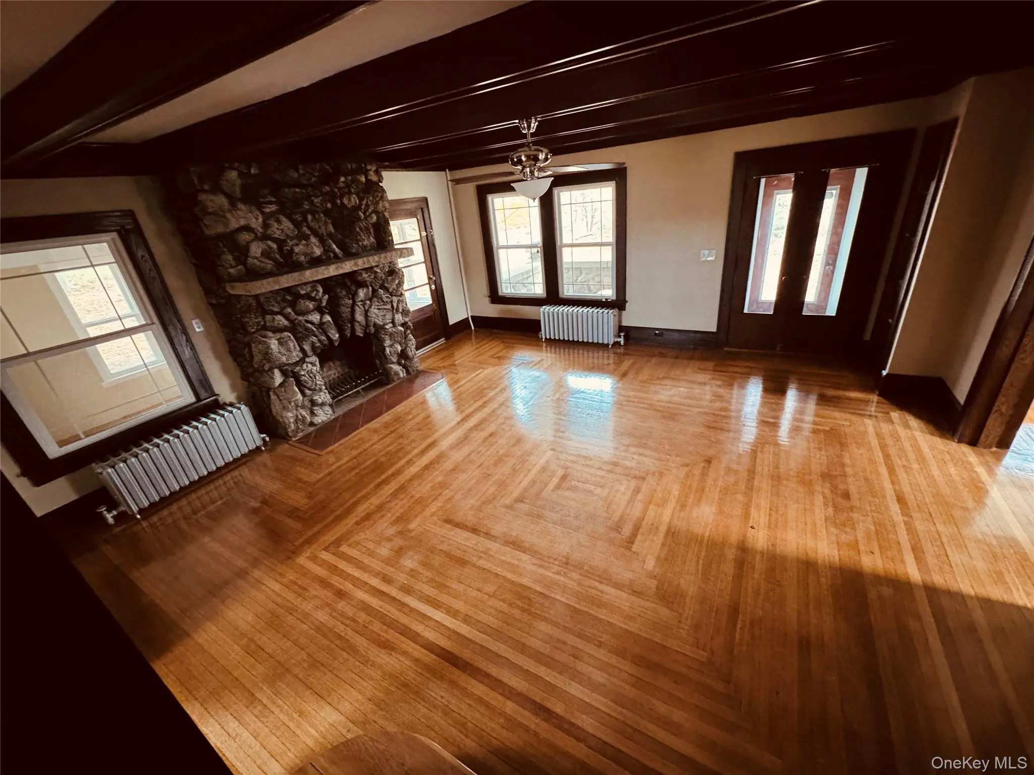 Unfurnished living room with radiator heating unit, beamed ceiling, and a fireplace Unfurnished living room with radiator heating unit, beamed ceiling, and a fireplace