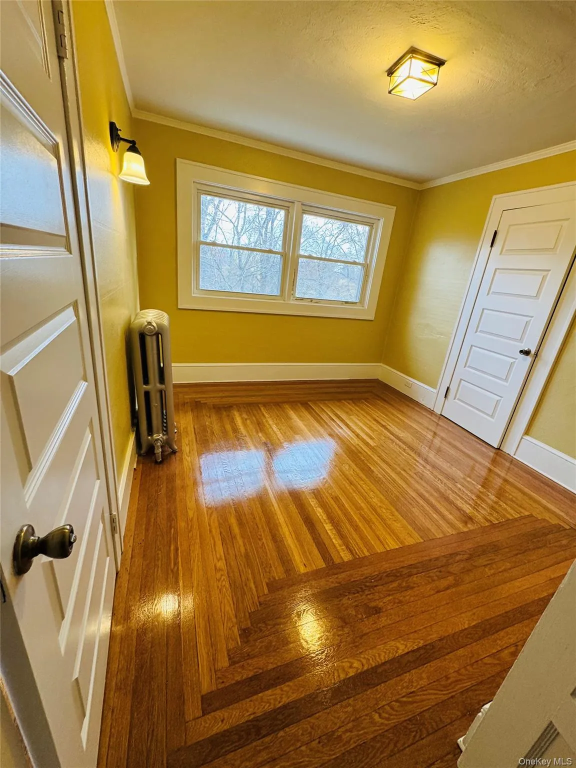 Unfurnished bedroom featuring crown molding, radiator heating unit, and light wood-type flooring Unfurnished bedroom featuring crown molding, radiator heating unit, and light wood-type flooring