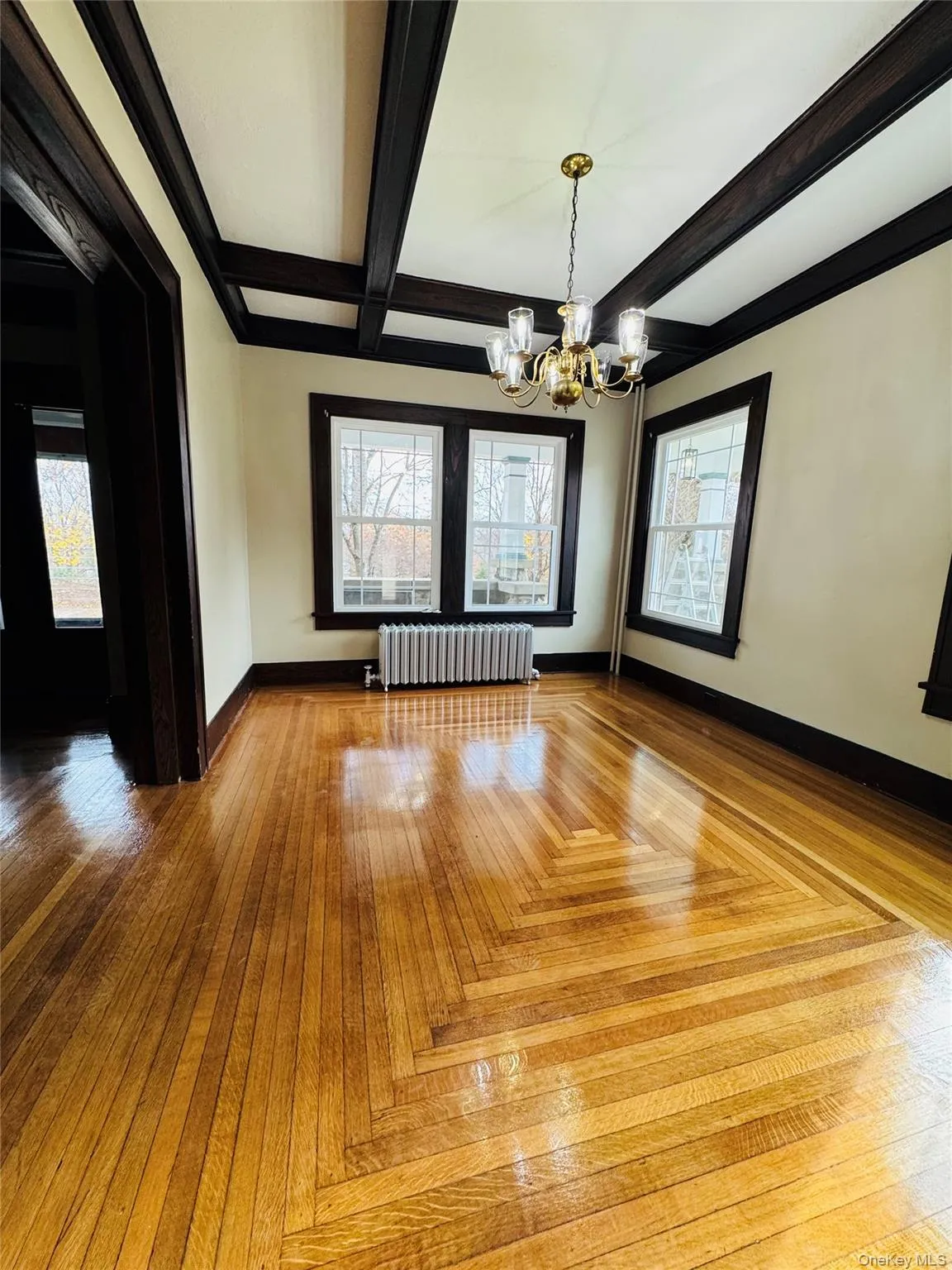 Spare room featuring beam ceiling, healthy amount of natural light, radiator heating unit, a chandelier, and coffered ceiling Spare room featuring beam ceiling, healthy amount of natural light, radiator heating unit, a chandelier, and coffered ceiling