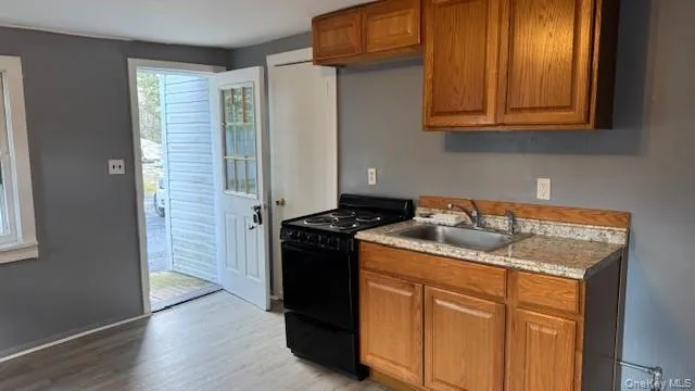 Kitchen with brown cabinets, black range with electric cooktop, light countertops, and light wood-style floors Kitchen with brown cabinets, black range with electric cooktop, light countertops, and light wood-style floors