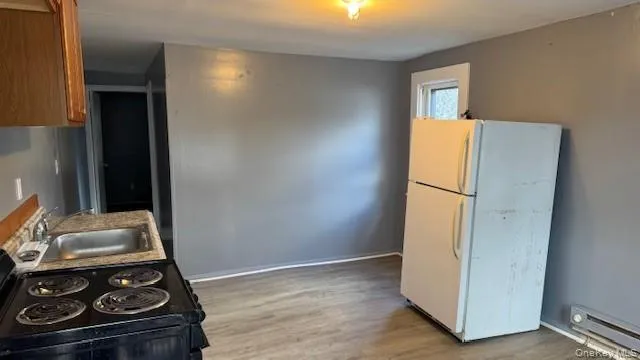 Kitchen with black range with electric cooktop, freestanding refrigerator, light wood finished floors, and a baseboard heating unit Kitchen with black range with electric cooktop, freestanding refrigerator, light wood finished floors, and a baseboard heating unit
