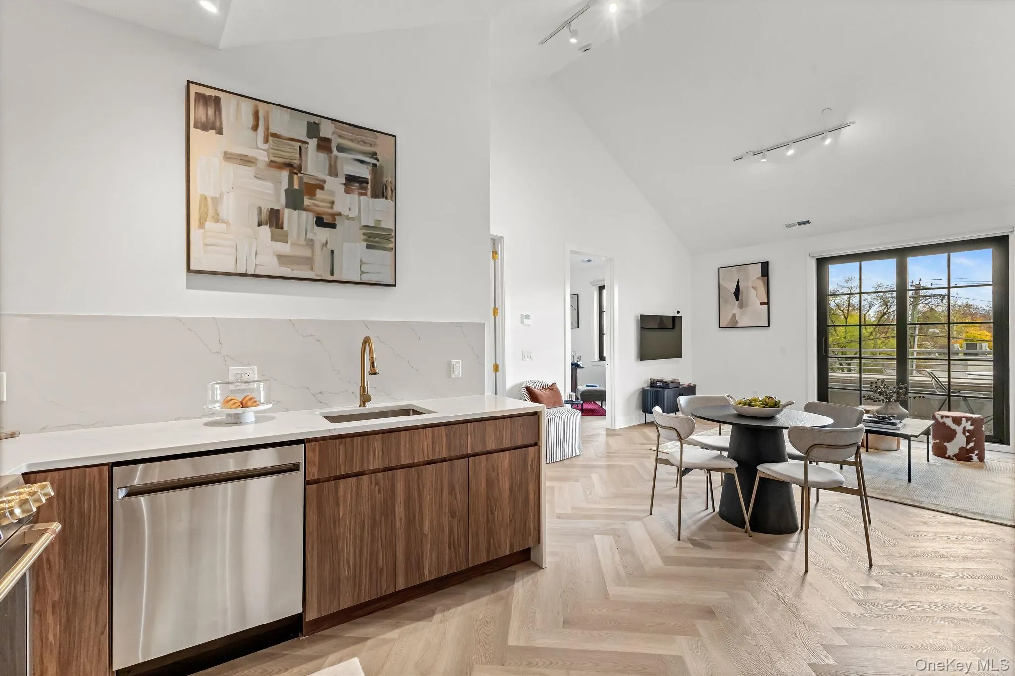 Kitchen with rail lighting, appliances with stainless steel finishes, tasteful backsplash, light stone counters, and high vaulted ceiling Kitchen with rail lighting, appliances with stainless steel finishes, tasteful backsplash, light stone counters, and high vaulted ceiling