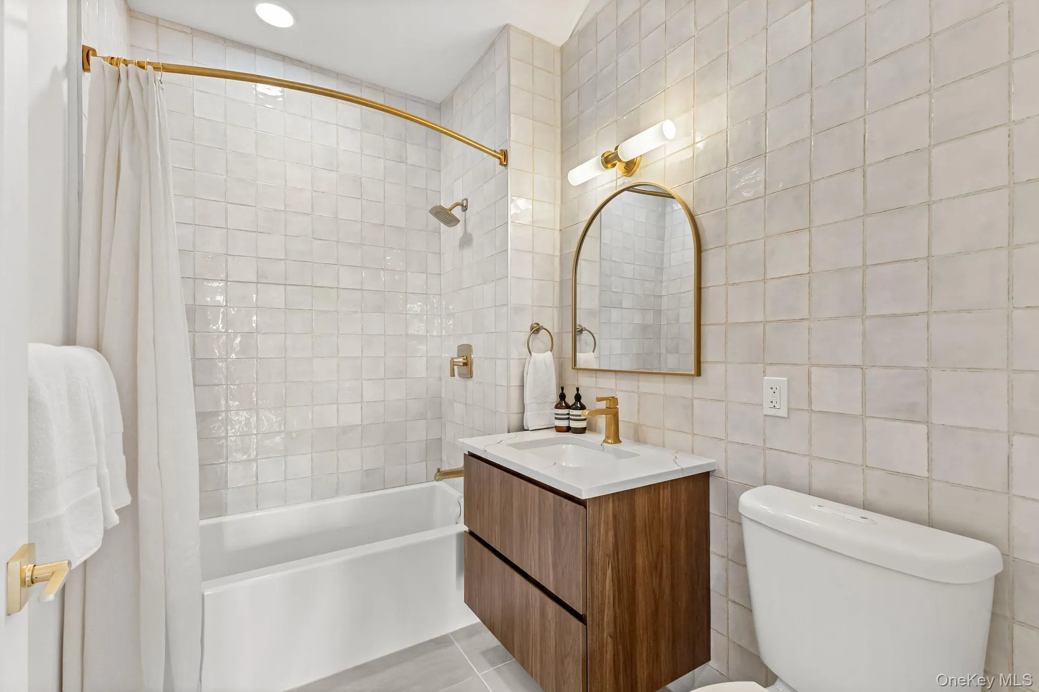 Bathroom with tile walls, shower / bath combination with curtain, vanity, and light tile patterned floors Bathroom with tile walls, shower / bath combination with curtain, vanity, and light tile patterned floors