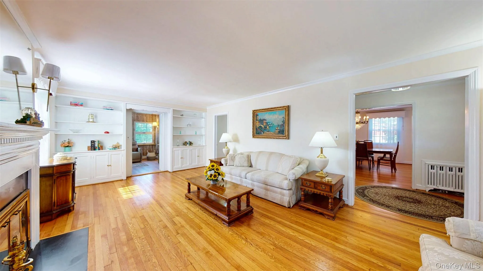 Living room featuring hardwood flooring, ceiling molding, a fireplace with black marble hearth and 2 built-in bookcases/cabinets Living room featuring hardwood flooring, ceiling molding, a fireplace with black marble hearth and 2 built-in bookcases/cabinets