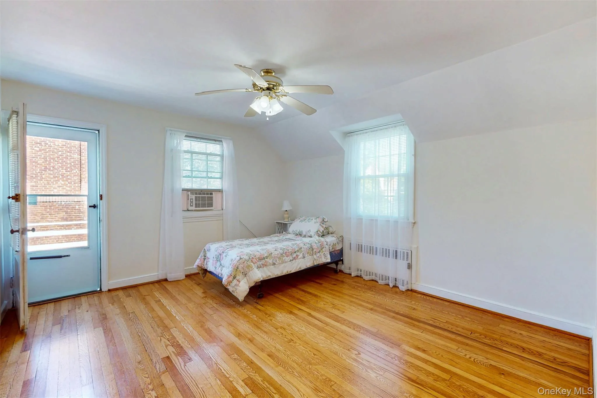 Large Bedroom #3 with door out to deck, recessed radiator, hardwood floors, cooling unit, and a ceiling fan Large Bedroom #3 with door out to deck, recessed radiator, hardwood floors, cooling unit, and a ceiling fan