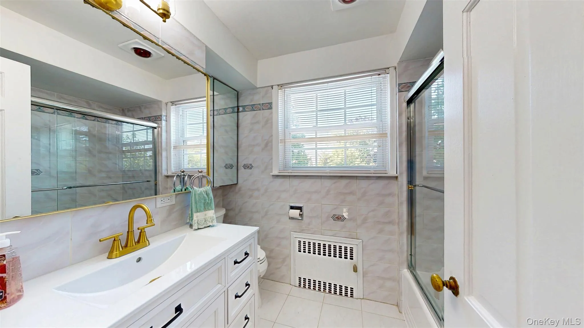 Bathroom featuring heat lamp/exhaust fan, recessed radiator, tile flooring, NEW vanity, tile walls, and combined bath / shower with glass door Bathroom featuring heat lamp/exhaust fan, recessed radiator, tile flooring, NEW vanity, tile walls, and combined bath / shower with glass door