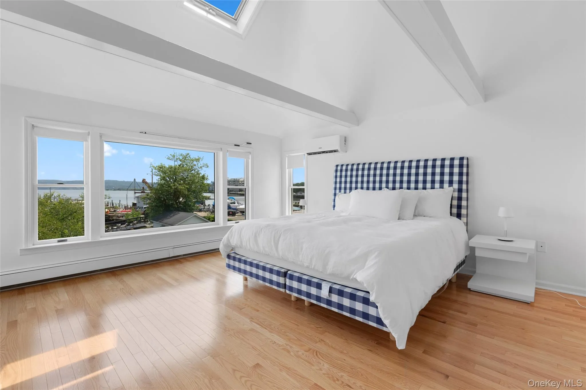 Bedroom with a skylight, light wood finished floors, a baseboard radiator, beamed ceiling, and a wall unit AC Bedroom with a skylight, light wood finished floors, a baseboard radiator, beamed ceiling, and a wall unit AC