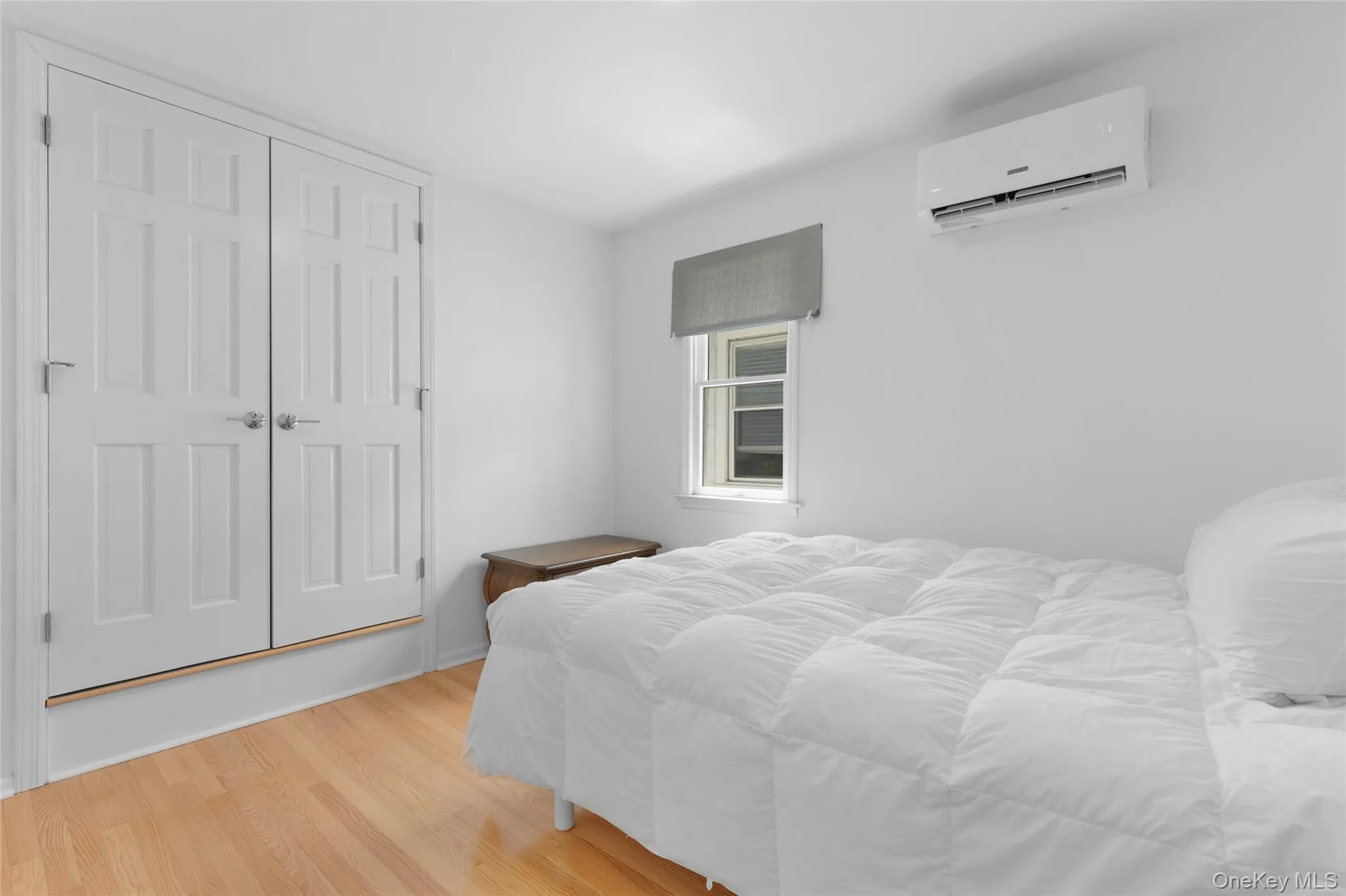 Bedroom featuring wood finished floors, a wall mounted AC, and a closet Bedroom featuring wood finished floors, a wall mounted AC, and a closet